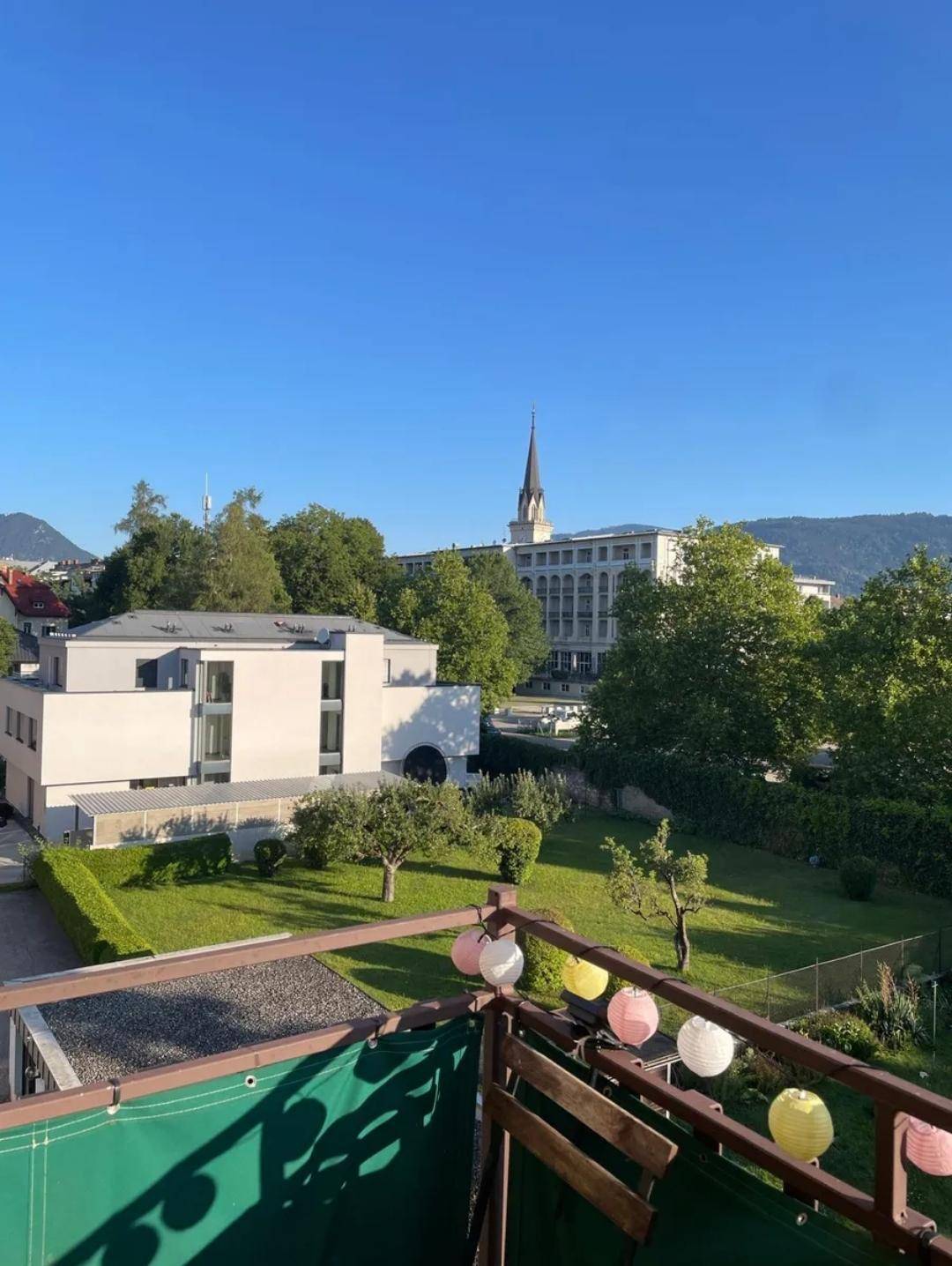 Heller Balkon mit weitem Blick über grüne Gärten und die Stadt bei Sonnenschein.