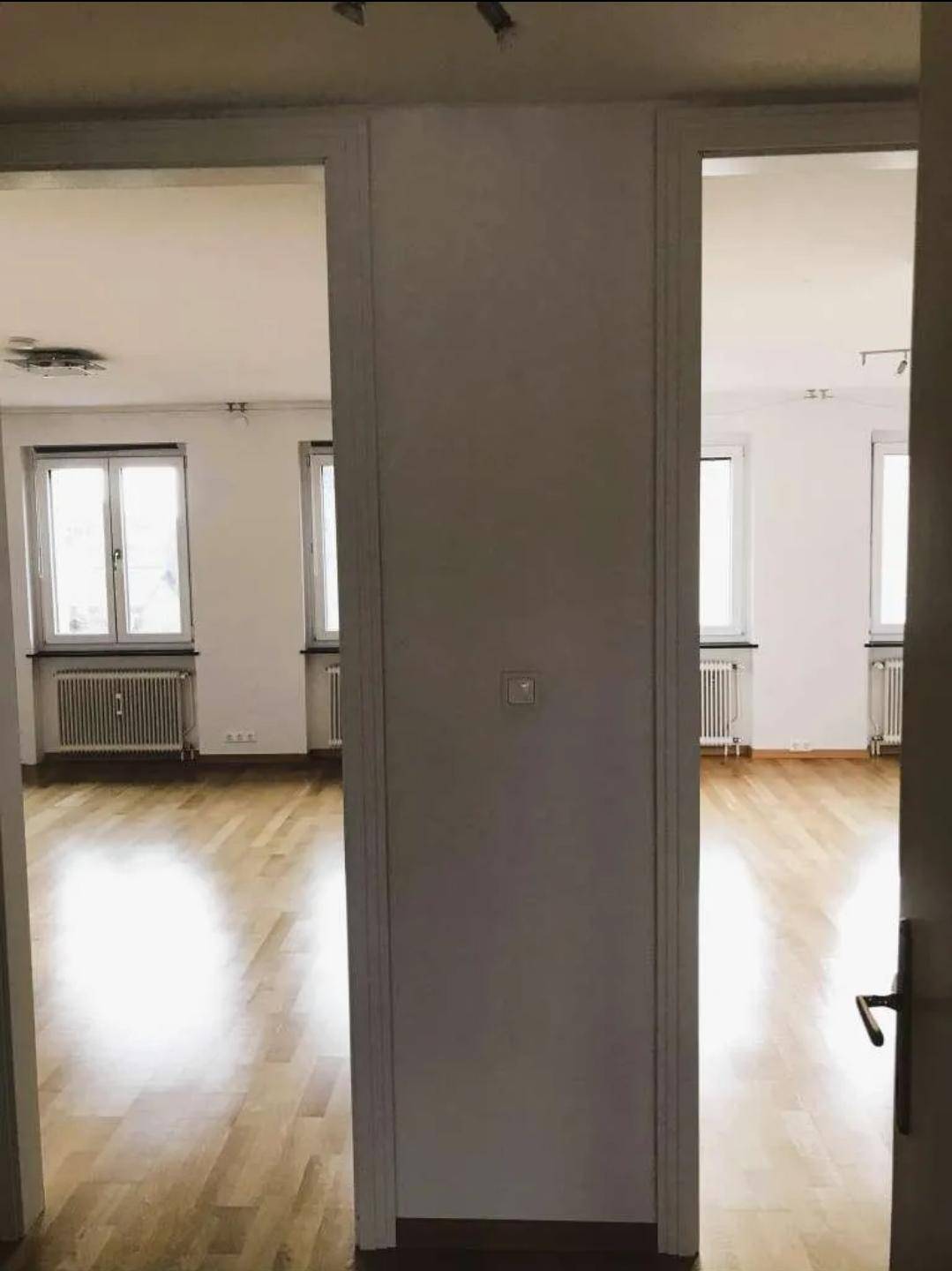 Durchgang zwischen zwei hellen Räumen mit durchgehendem Holzboden und Fenstern.