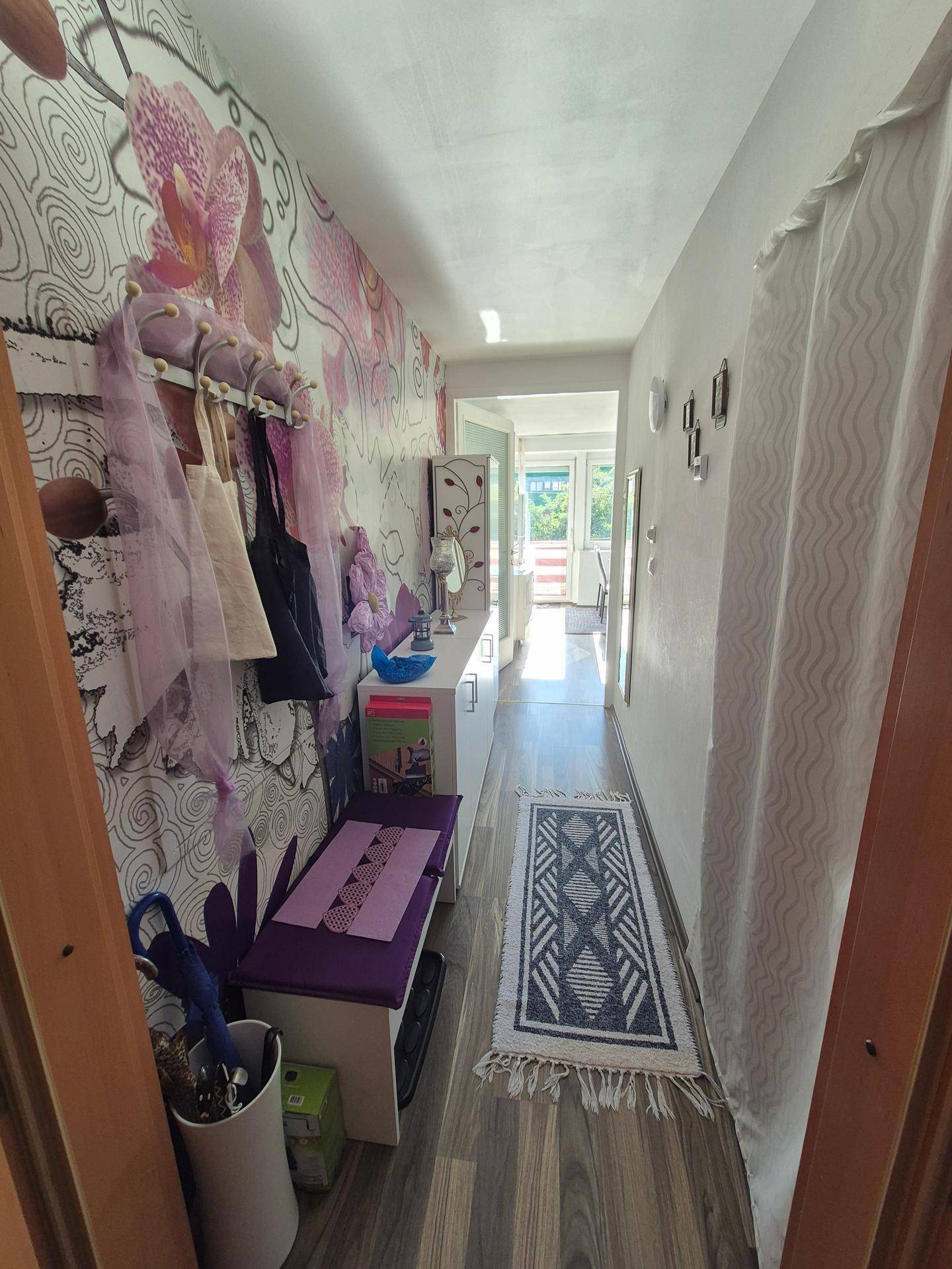 Langer Flur mit auffälliger Orchideen-Tapete, Garderobe und praktischer Sitzbank.
