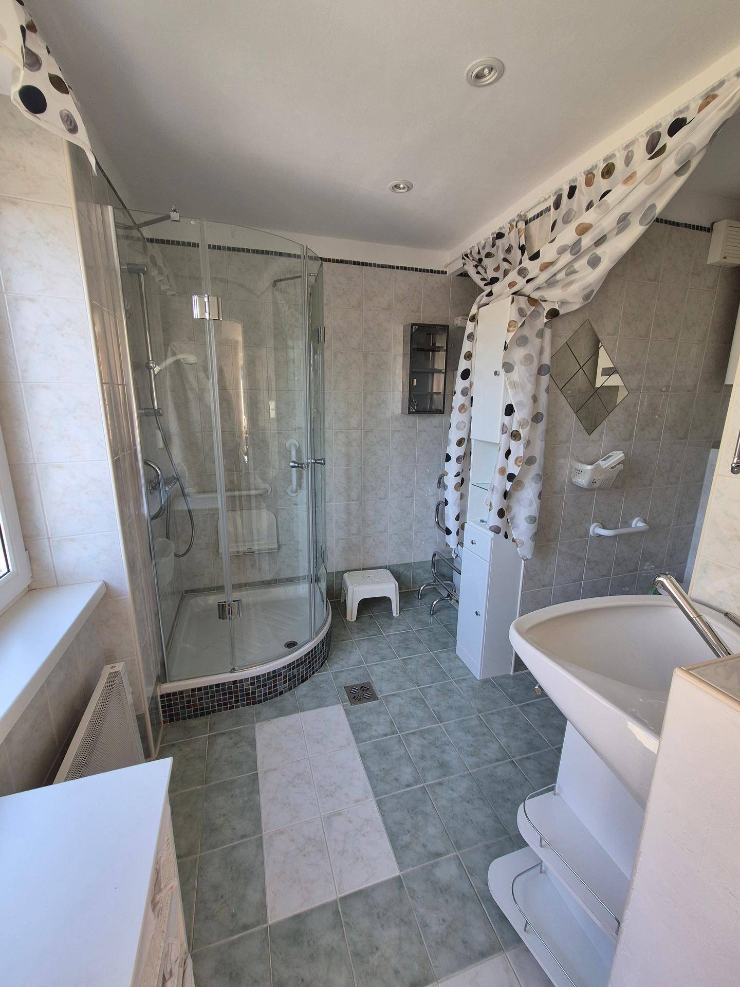 Helles Badezimmer mit Eckdusche, Waschbecken und hellgrünen Fliesen.