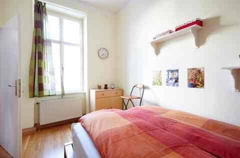 Helles Schlafzimmer mit Holzboden, großem Fenster und einfacher Einrichtung.