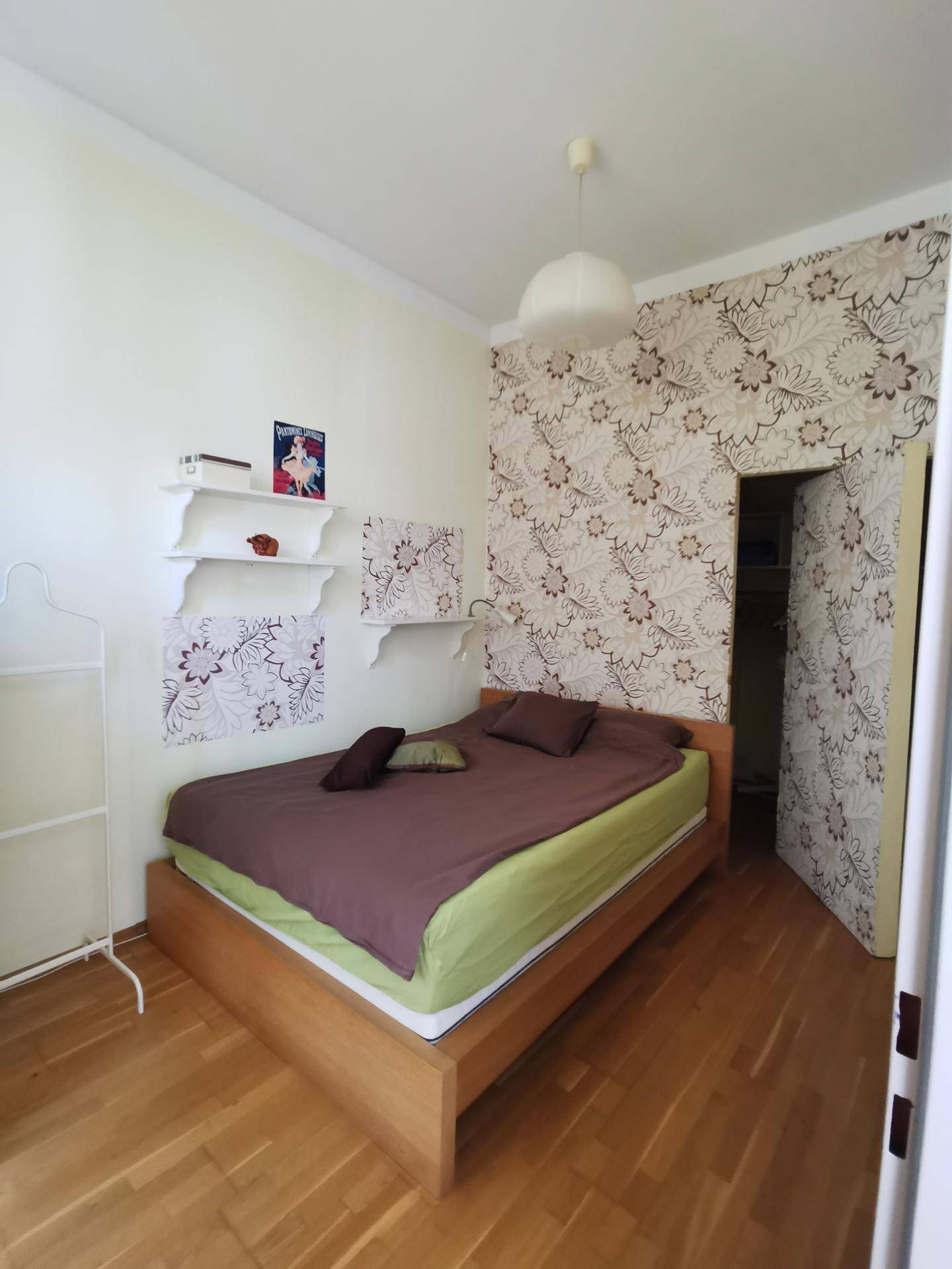 Schlafzimmer mit Holzbett, gemusterter Tapete und hellem Parkettboden.