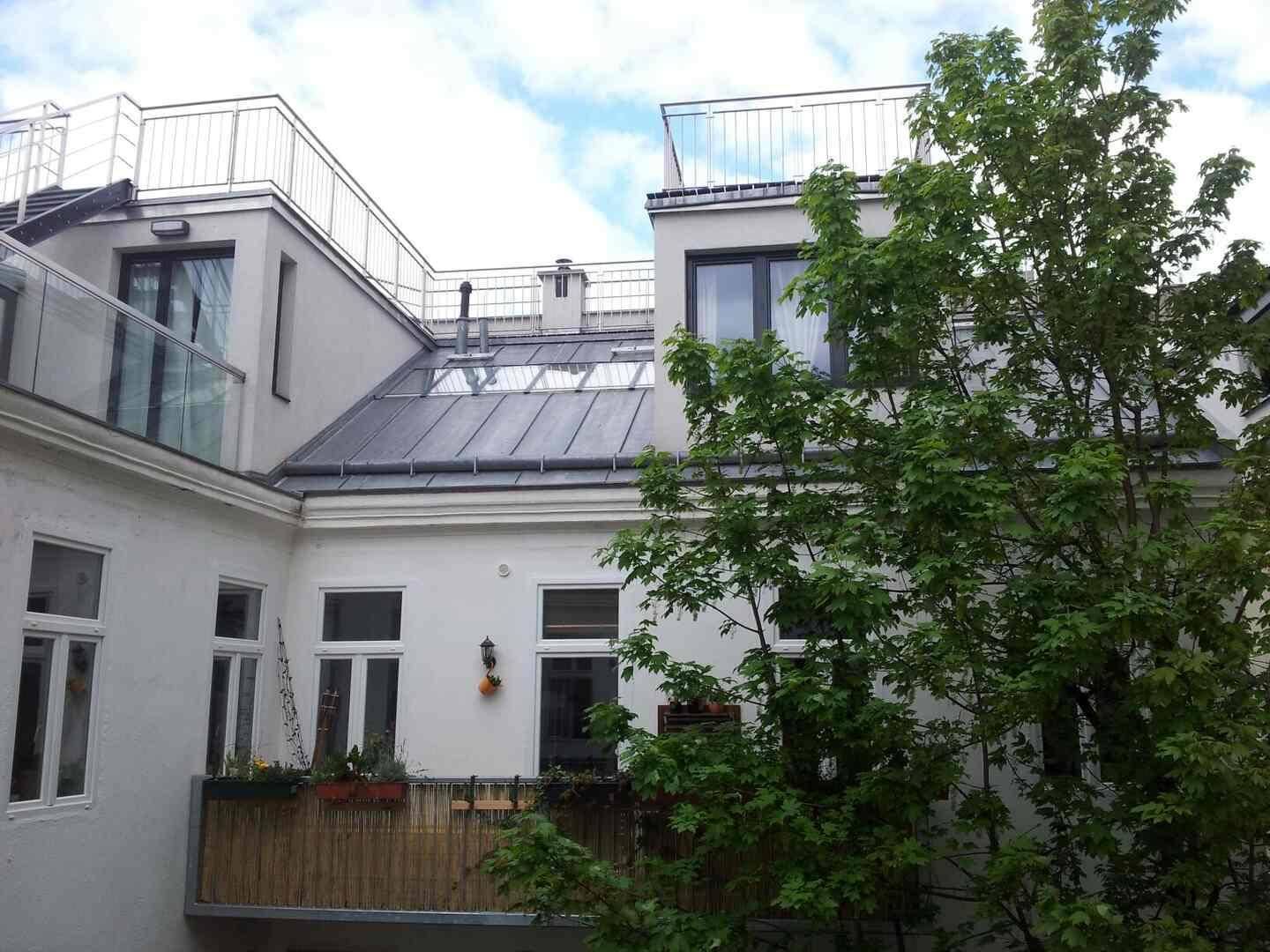 Blick auf den Innenhof mit einem Balkon, umgeben von Bäumen und weiteren Dachterrassen.