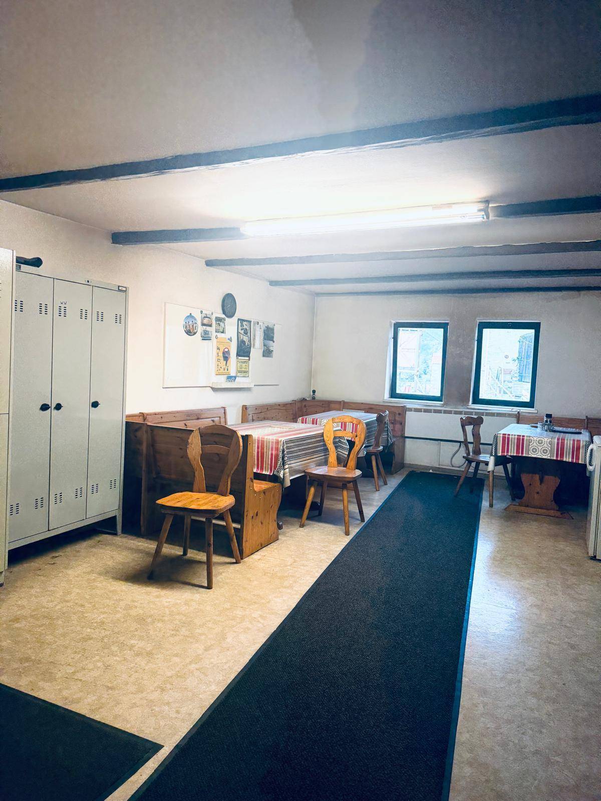 Gemütlicher Pausenraum mit Holztischen, Bänken und Spinden für Mitarbeiter, mit sichtbaren Deckenbalken.