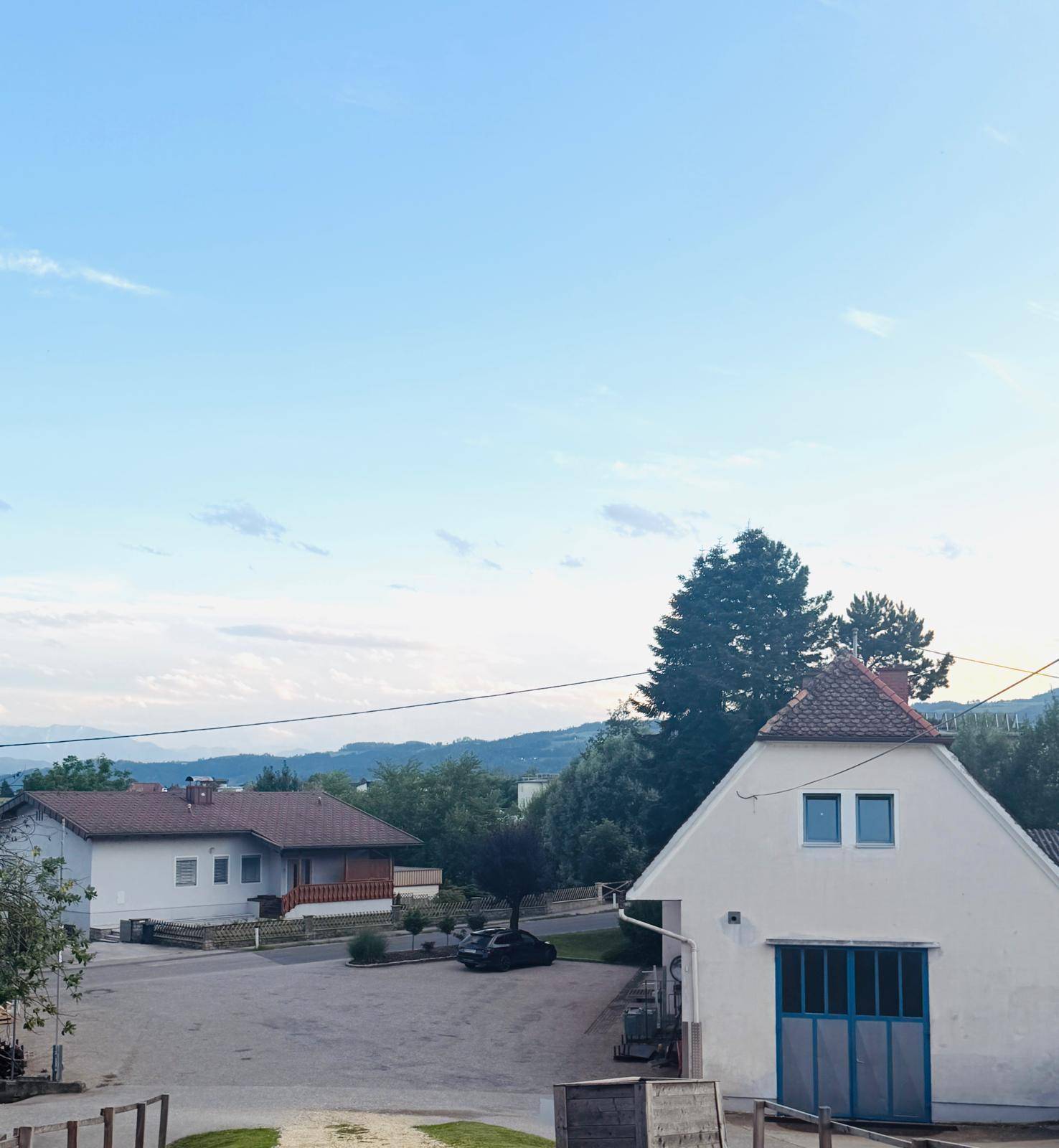 Gebäude mit blauen Türen und Fenstern, umgeben von weiteren Häusern und einer bergigen Landschaft im Hintergrund.