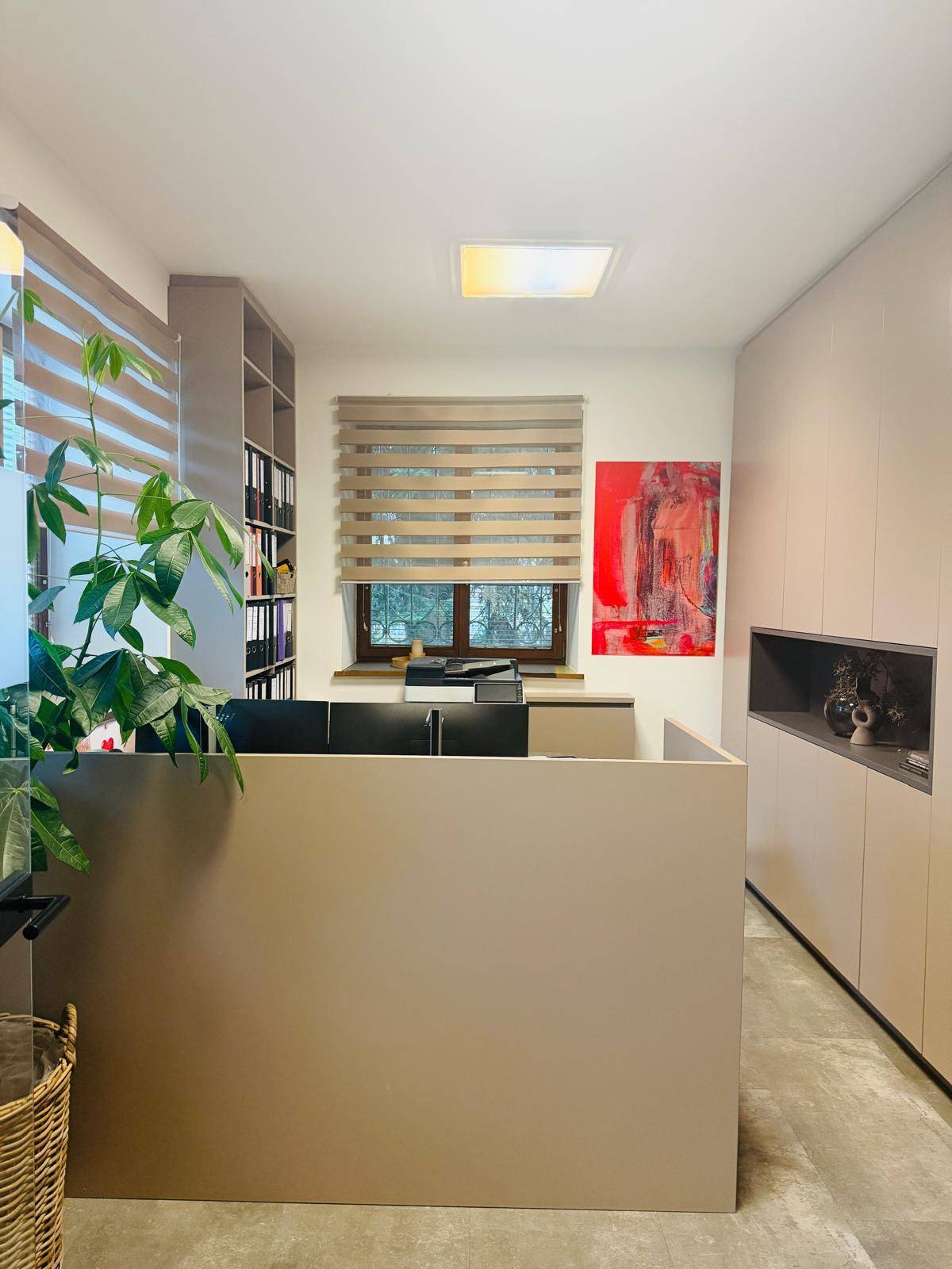 Helles Büro mit modernen Möbeln, Regalen und einem dekorativen roten Bild an der Wand, gut organisiert.