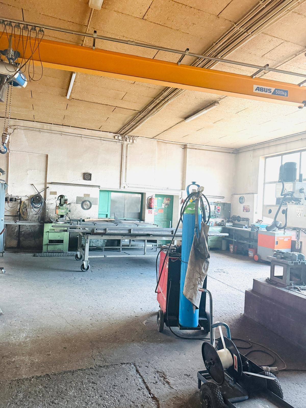 Industrielle Werkstatt mit Krananlage, Schweißgeräten und verschiedenen Arbeitsbereichen für Metallverarbeitung.