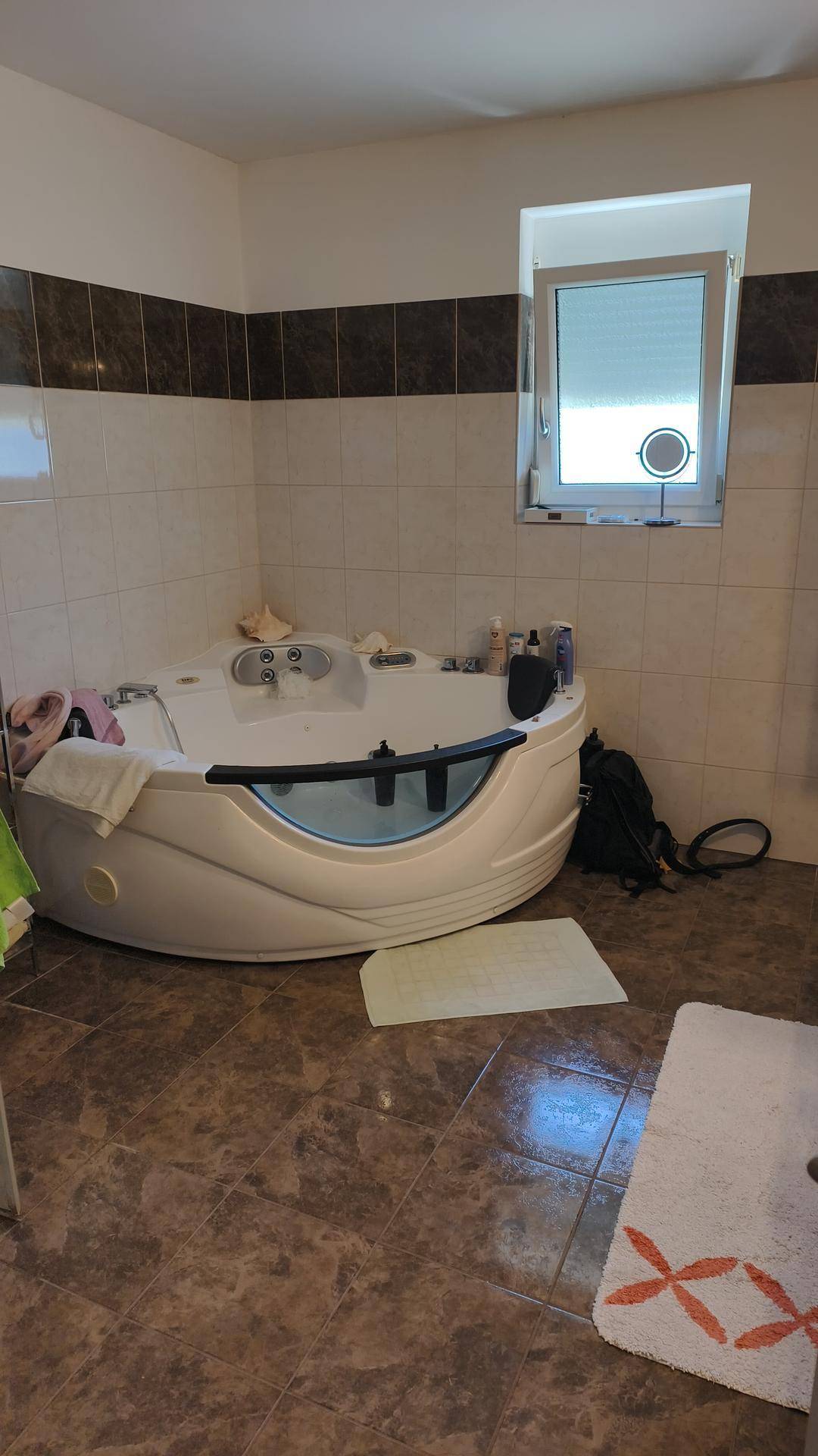 Geräumiges Badezimmer mit Eck-Whirlpool, Fliesenboden und einem Fenster für Tageslicht.