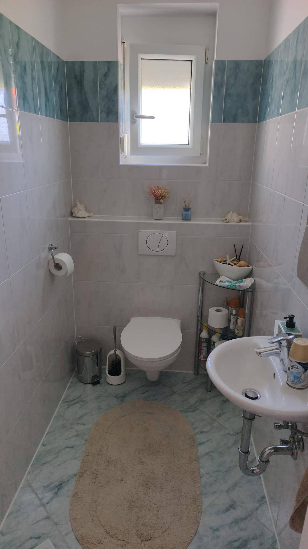 Kleines WC mit Wand-WC, Waschbecken und einem Fenster für natürliche Belüftung.
