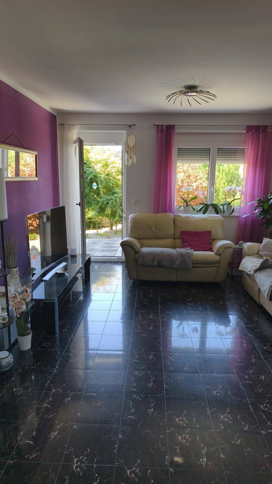Helles Wohnzimmer mit dunklen Fliesen, lila Wänden und Zugang zum Gartenbereich.