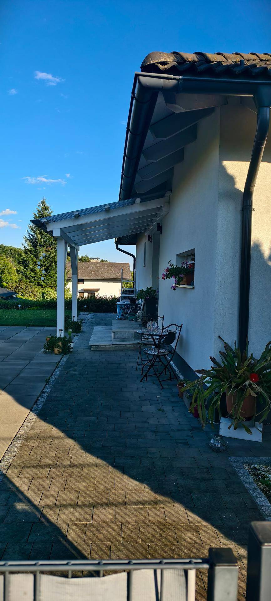 Überdachte Terrasse mit Sitzgelegenheiten und gepflastertem Bereich neben dem Haus.