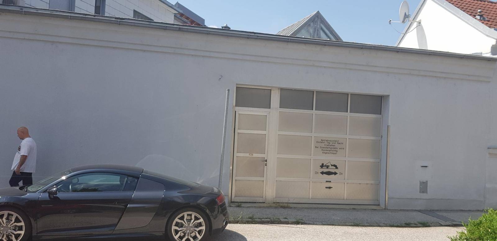 Außenansicht einer Garageneinfahrt mit einem geparkten Sportwagen und einer Person.