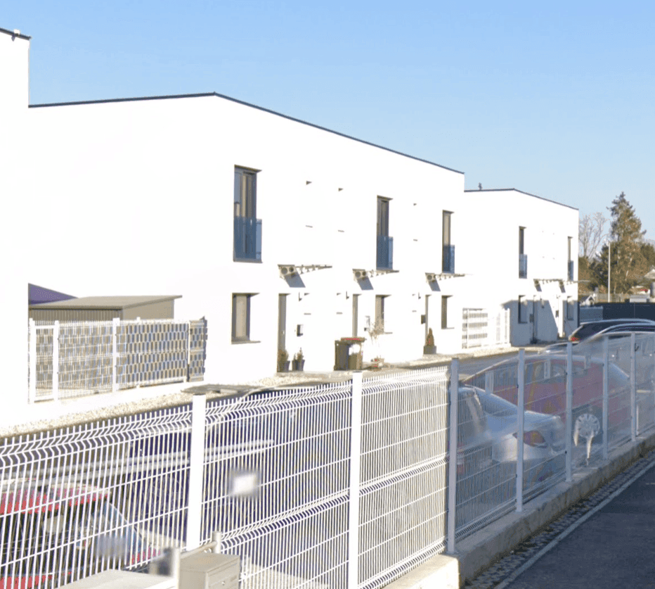 Reihenhäuser mit weißer Fassade, modernen Fenstern und flachem Dach entlang einer Straße.