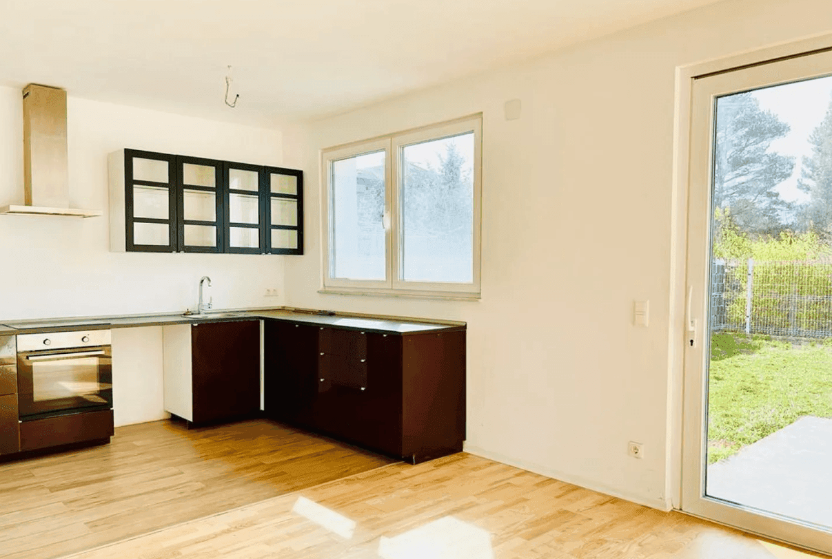 Helle Küche mit Parkettboden, Fenster und vorbereiteten Anschlüssen für eine Einbauküche.