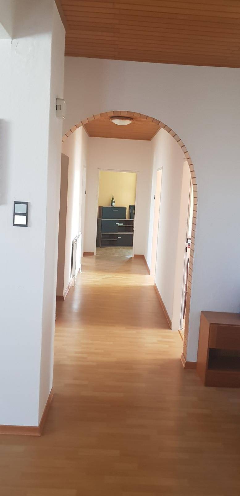 Flur mit Holzfußboden und einem Rundbogen, der zu einem weiteren Raum führt.