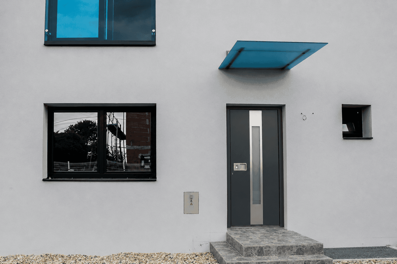 Nahaufnahme des modernen Hauseingangs mit dunkler Tür, Überdachung und Fenster im Erdgeschoss.