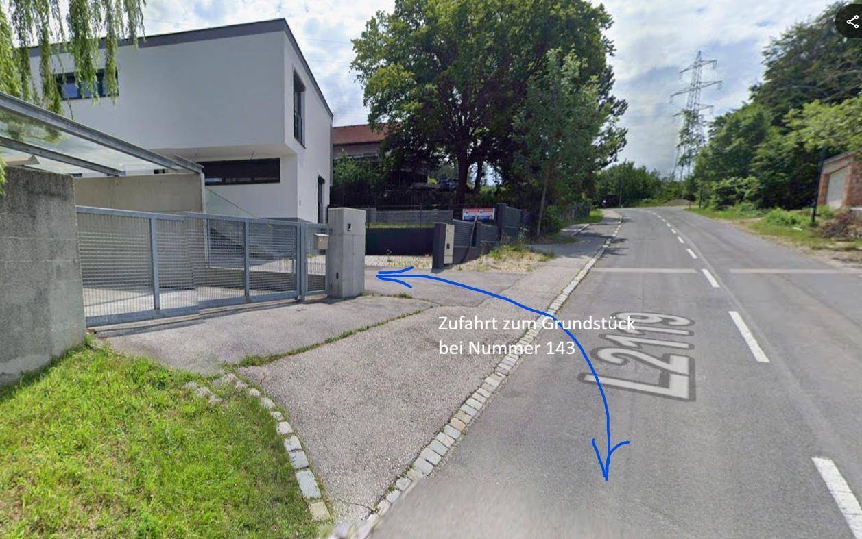 Zufahrt zu einem modernen Gebäude mit Tor und Hinweisschild an einer Landstraße.