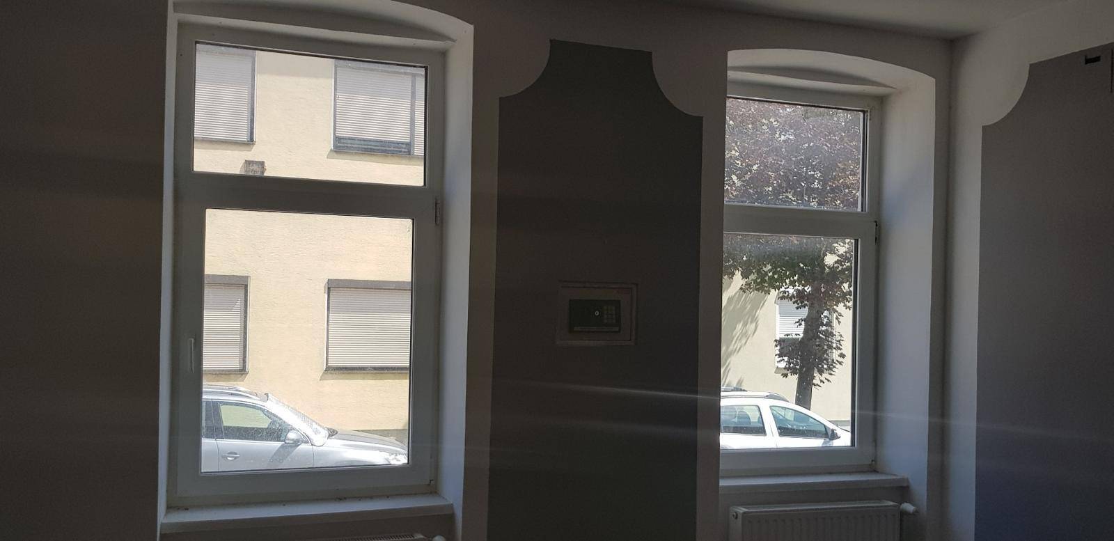Zwei Fenster in einem Raum mit Blick auf die Straße und gegenüberliegende Gebäude.