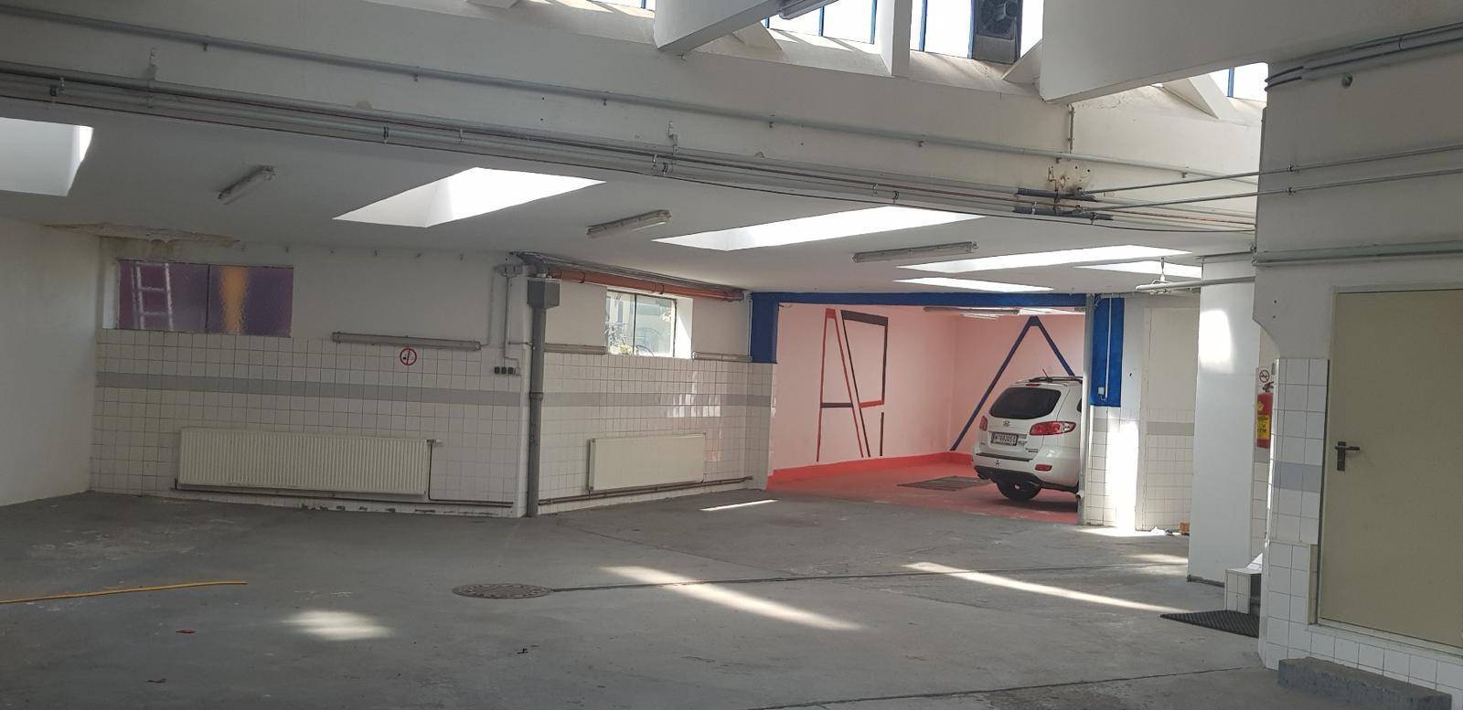 Großer leerer Raum, möglicherweise eine Garage oder Werkstatt, mit Oberlichtern und gefliesten Wänden.