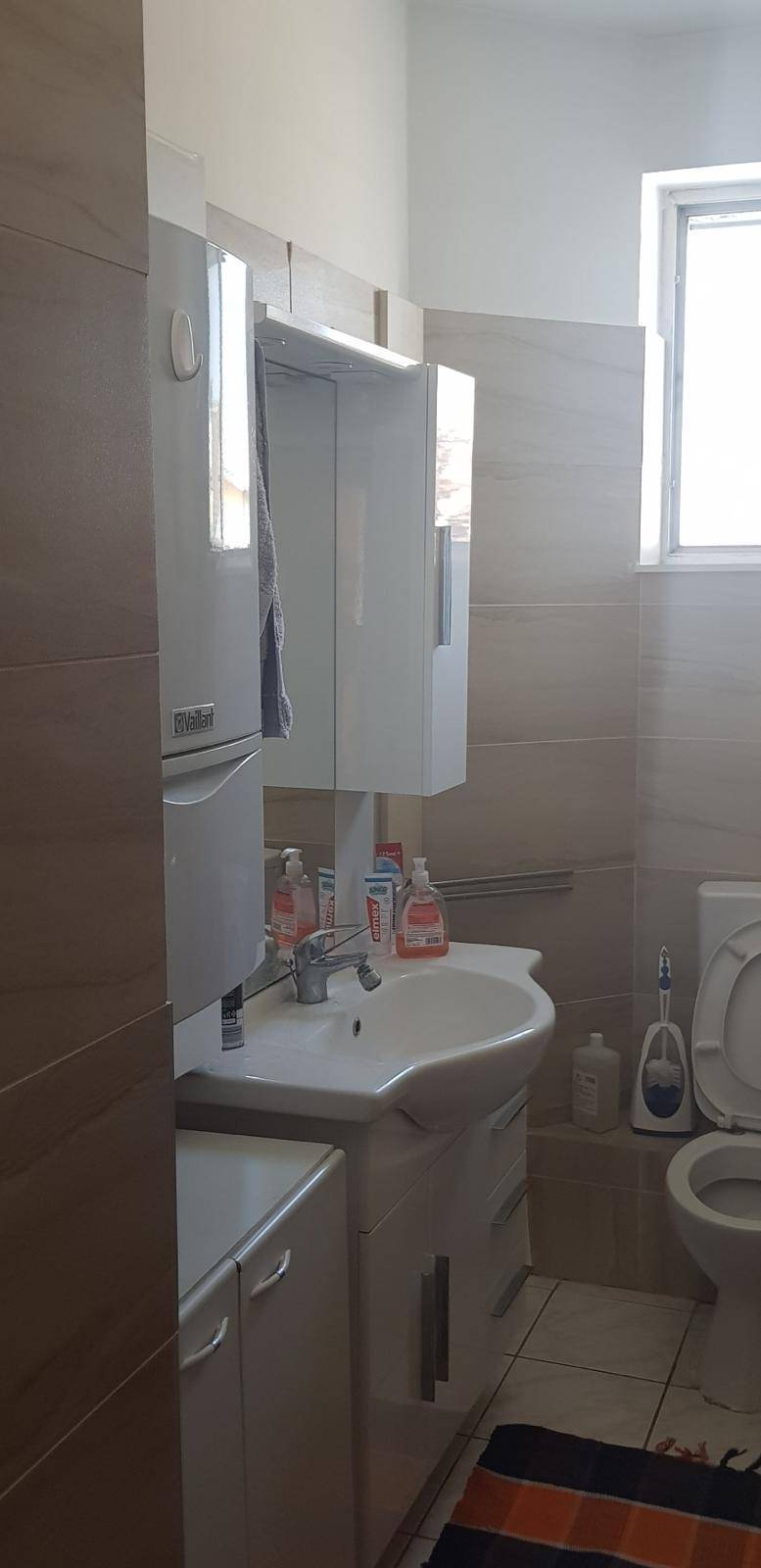 Badezimmer mit Waschbecken, Spiegelschrank, Toilette und einem Fenster für Tageslicht.