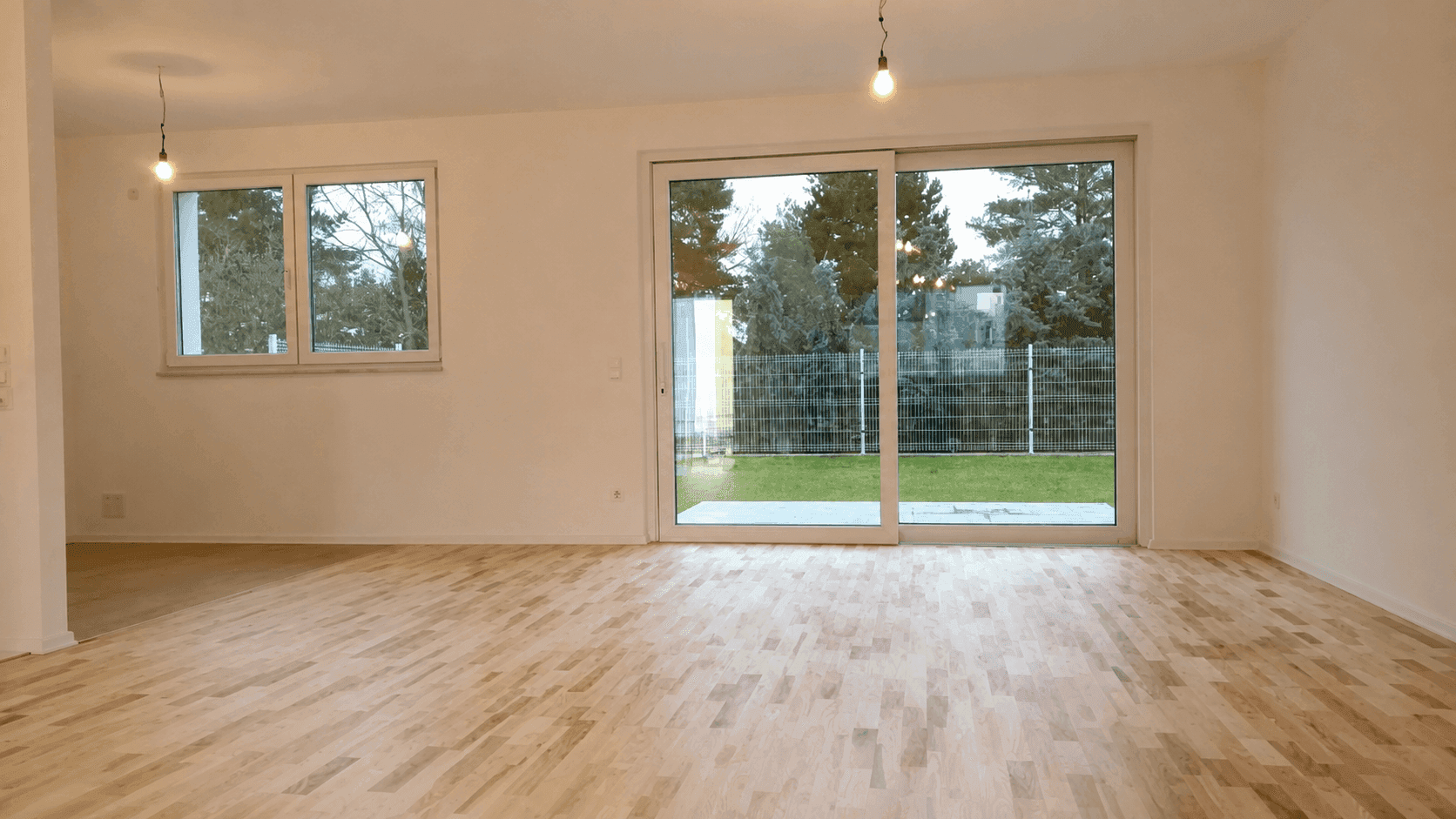 Geräumiges Wohnzimmer mit hellem Parkettboden und großen Schiebetüren zum Gartenbereich.