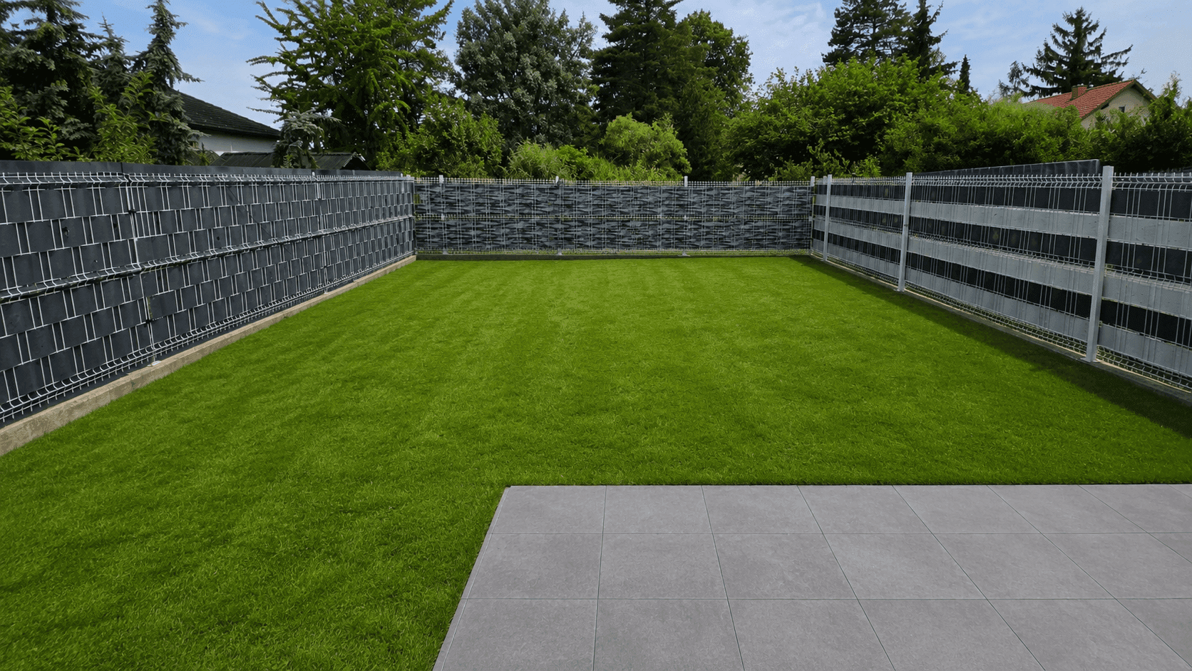 Gepflegter Garten mit Rasenfläche und einer gepflasterten Terrasse, umgeben von einem Zaun.