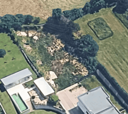 Luftaufnahme eines unbebauten Grundstücks, umgeben von weiteren Gebäuden und landwirtschaftlichen Flächen.