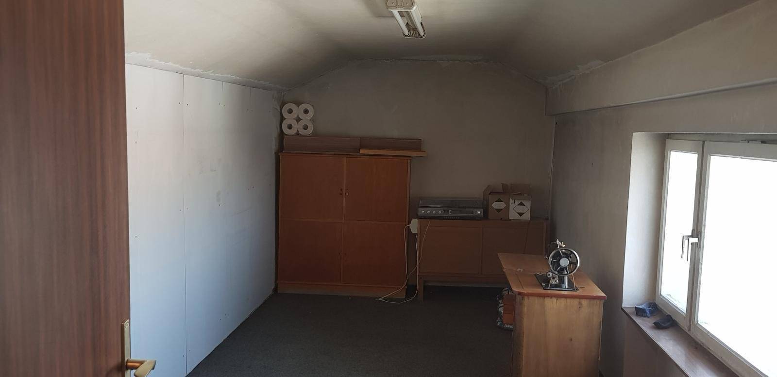 Dachzimmer mit schräger Decke, Fenster und einfacher Einrichtung, genutzt als Abstellraum.