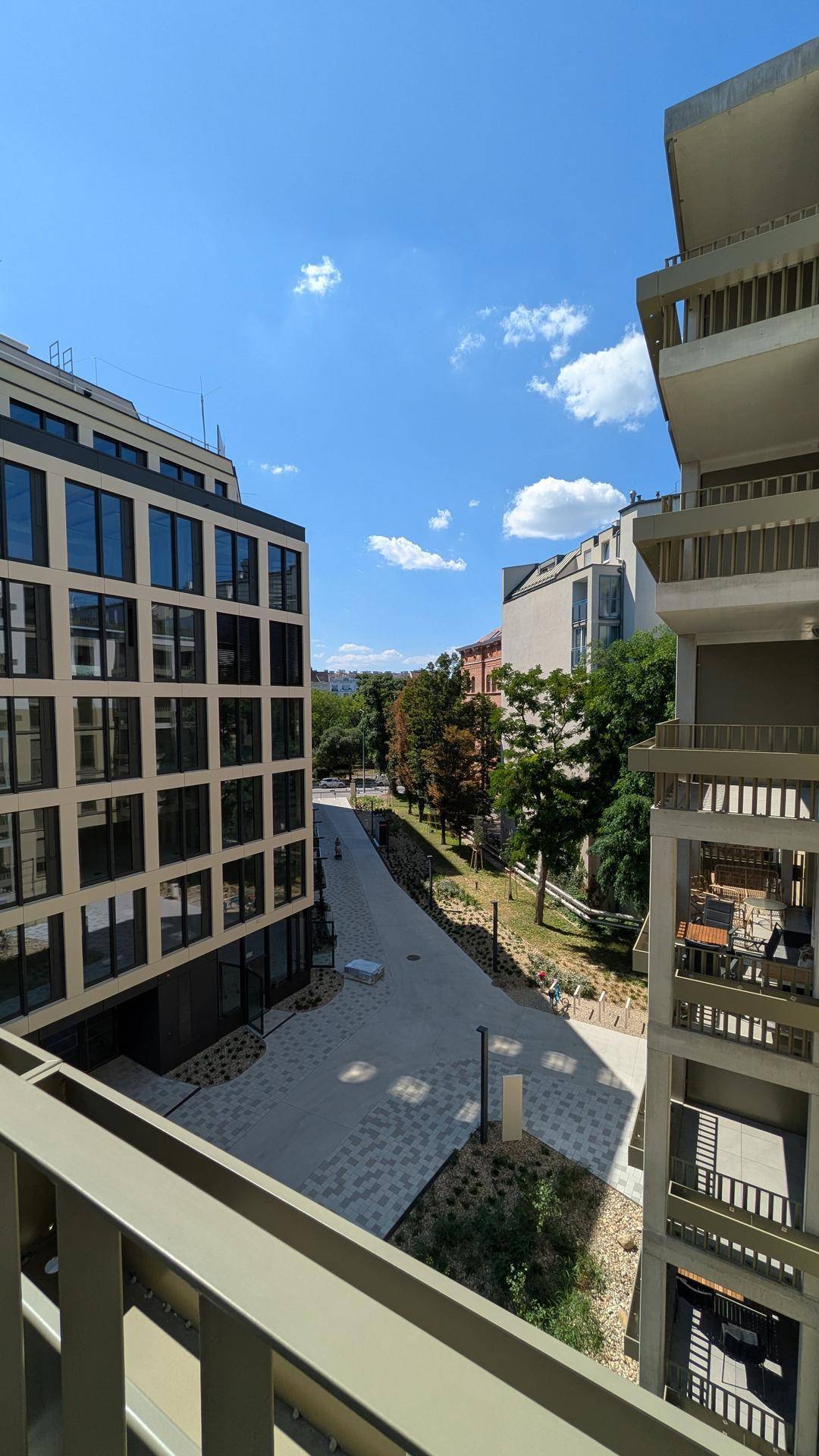 Sonniger Ausblick von einem Balkon auf die moderne Architektur und die grünen Außenanlagen.