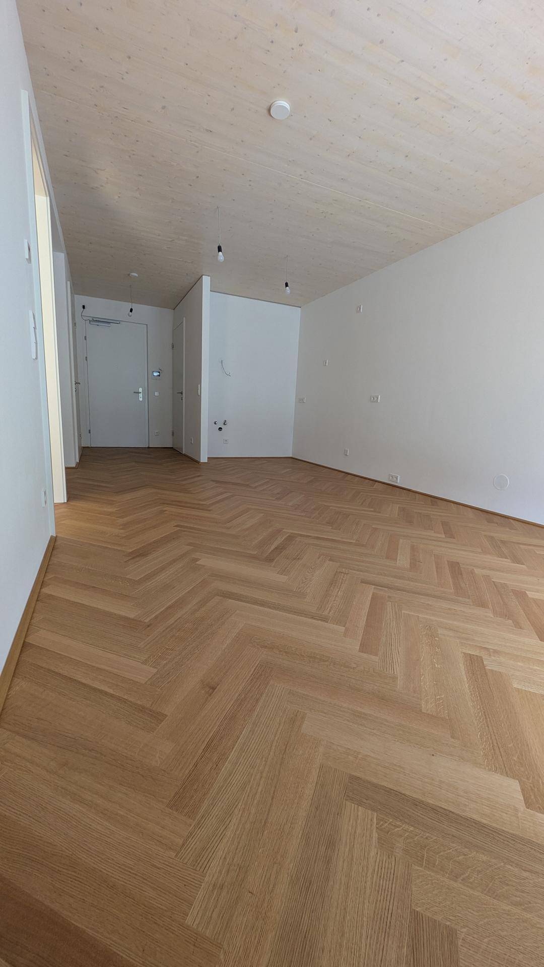 Geräumiger Flur mit hellem Fischgrätparkett und Holzbalkendecke in einem modernen Neubau.