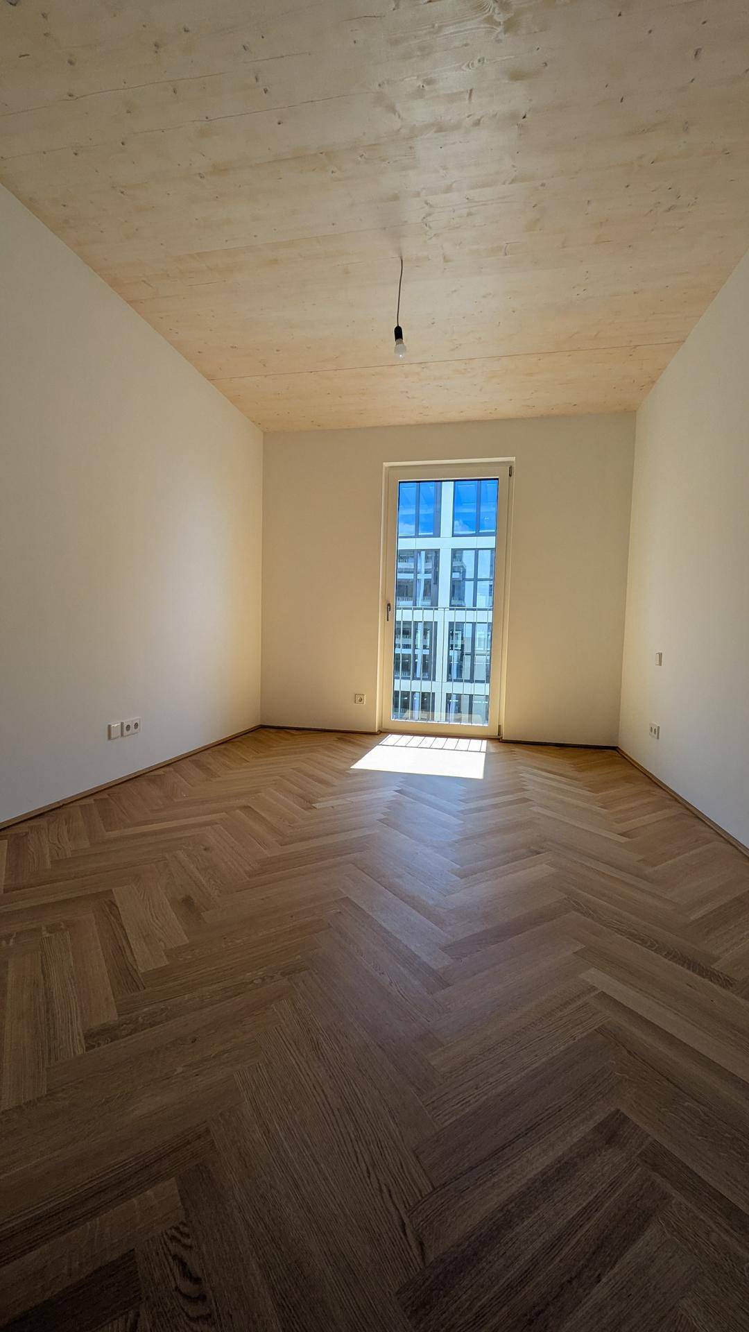 Lichtdurchflutetes Schlafzimmer mit Fischgrätparkett, Holzbalkendecke und großem Fenster.