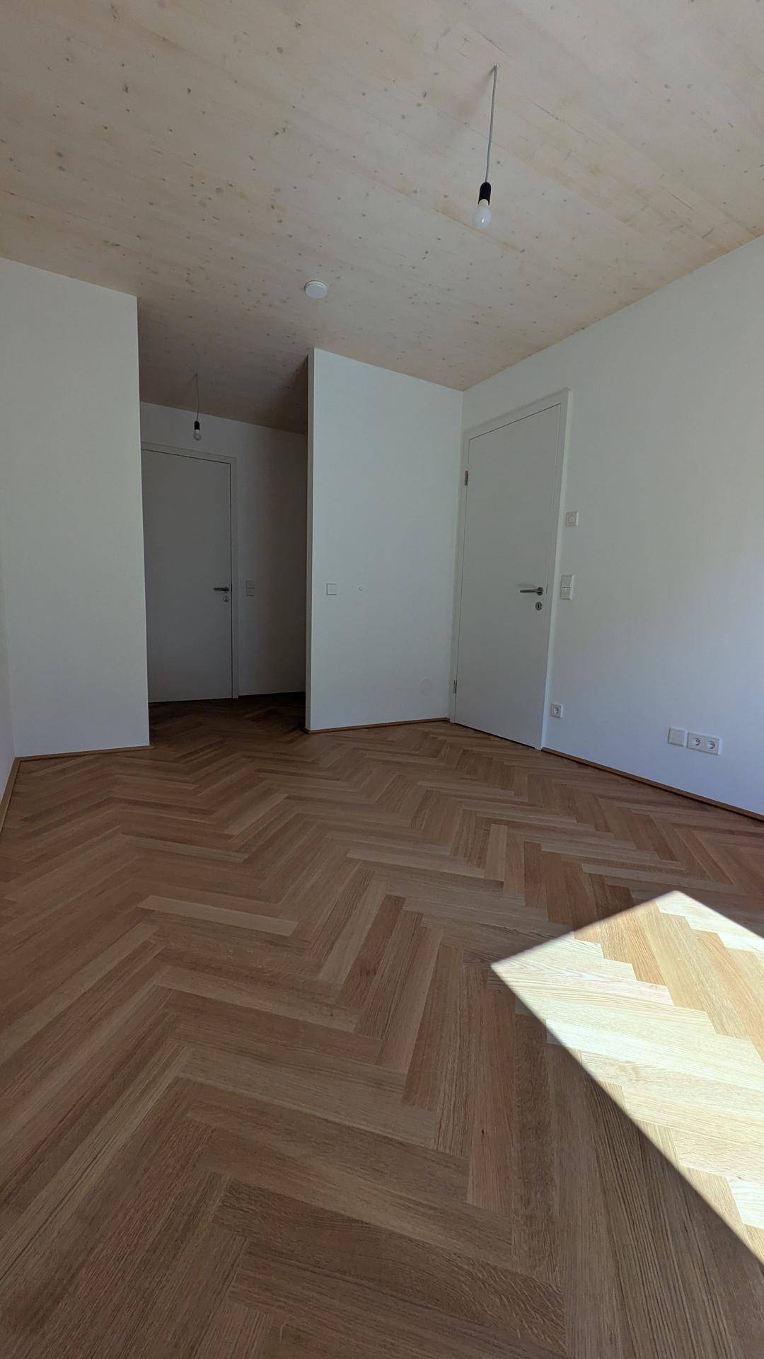 Heller Eingangsbereich mit Fischgrätparkett, Holzbalkendecke und weißen Türen in einem Neubau.