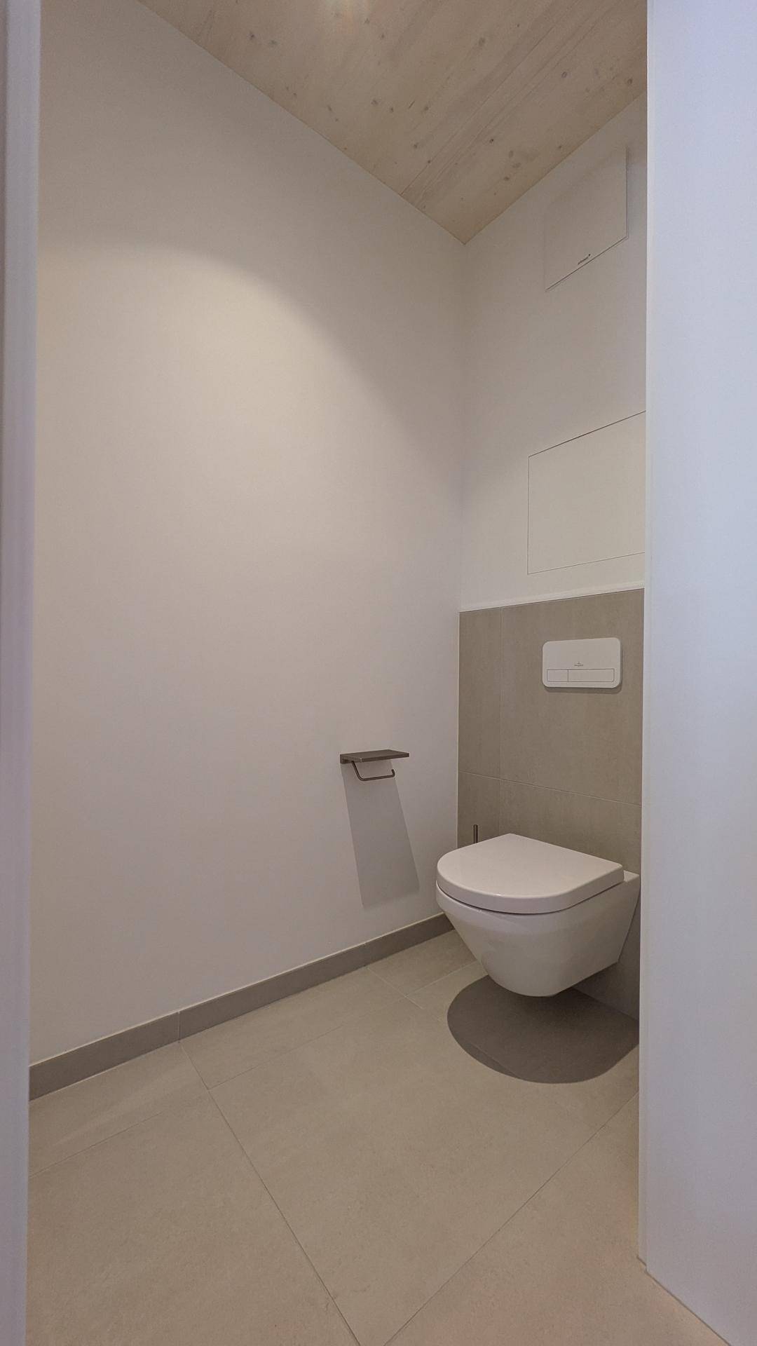 Separates Gäste-WC mit wandhängender Toilette und modernen Fliesen in einem Neubau.