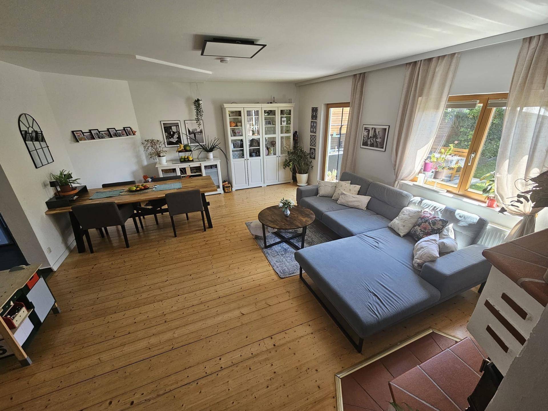 Geräumiger offener Wohn-Essbereich mit Holzboden, großem Sofa und Esstisch, hell und einladend.
