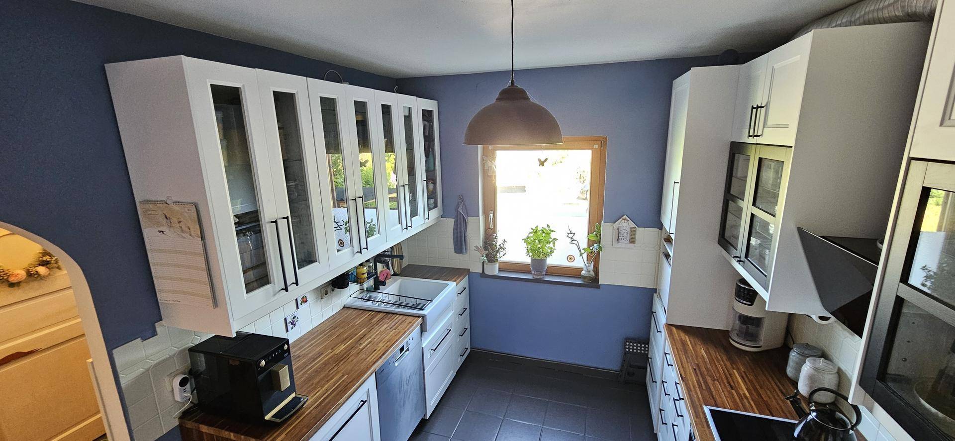 Funktionale Küche mit weißen Schränken, Holz-Arbeitsplatten und blauen Wänden, gut beleuchtet durch ein Fenster.