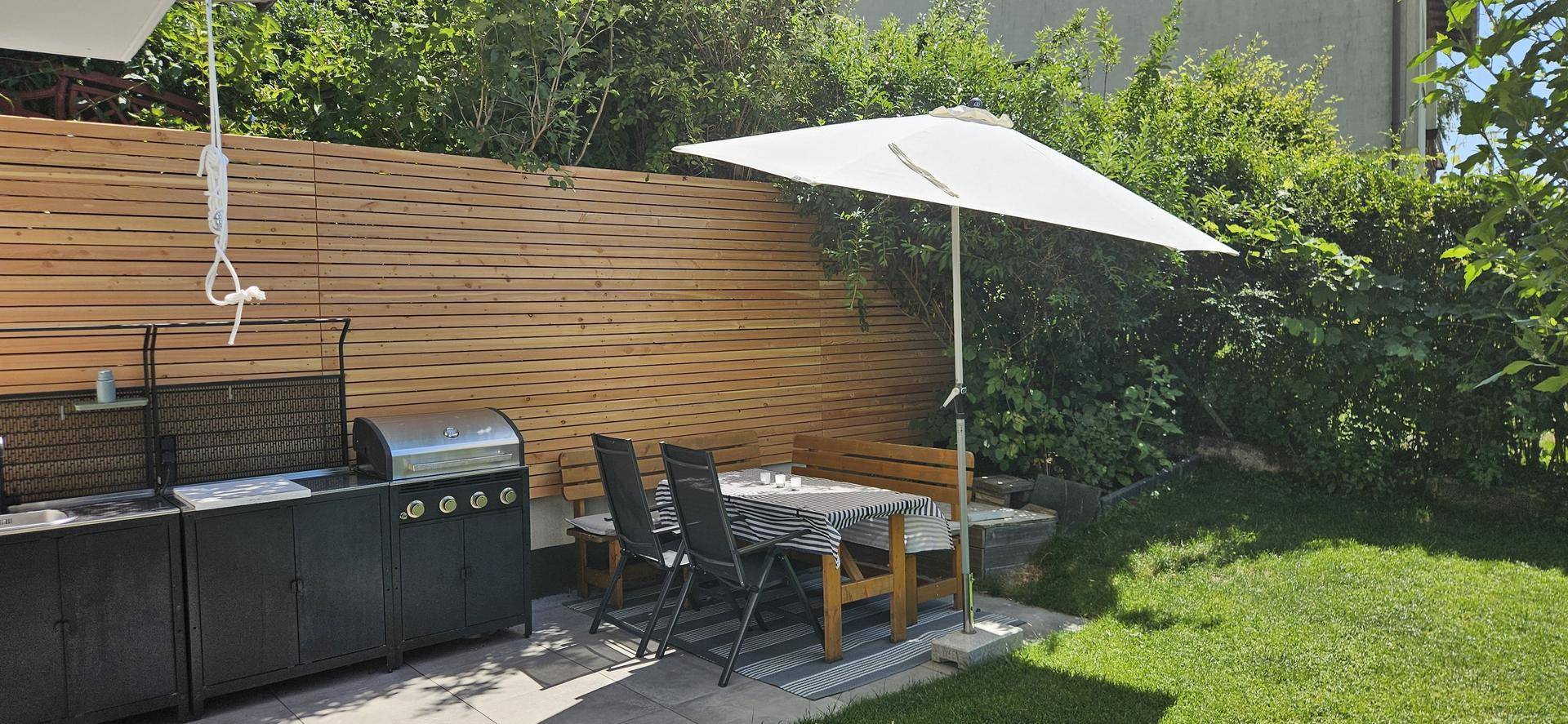 Gemütlicher Gartenbereich mit Grillstation, Esstisch und Sonnenschirm für entspannte Stunden.