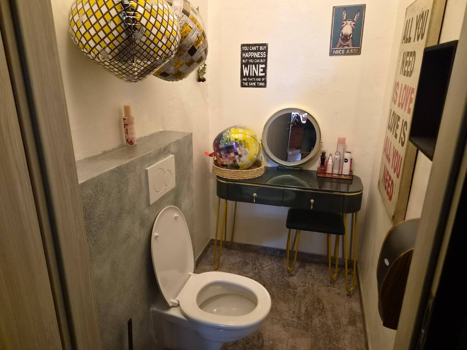 Toilettenraum mit wandhängendem WC, Spiegel und dekorativen Elementen wie Discokugeln.