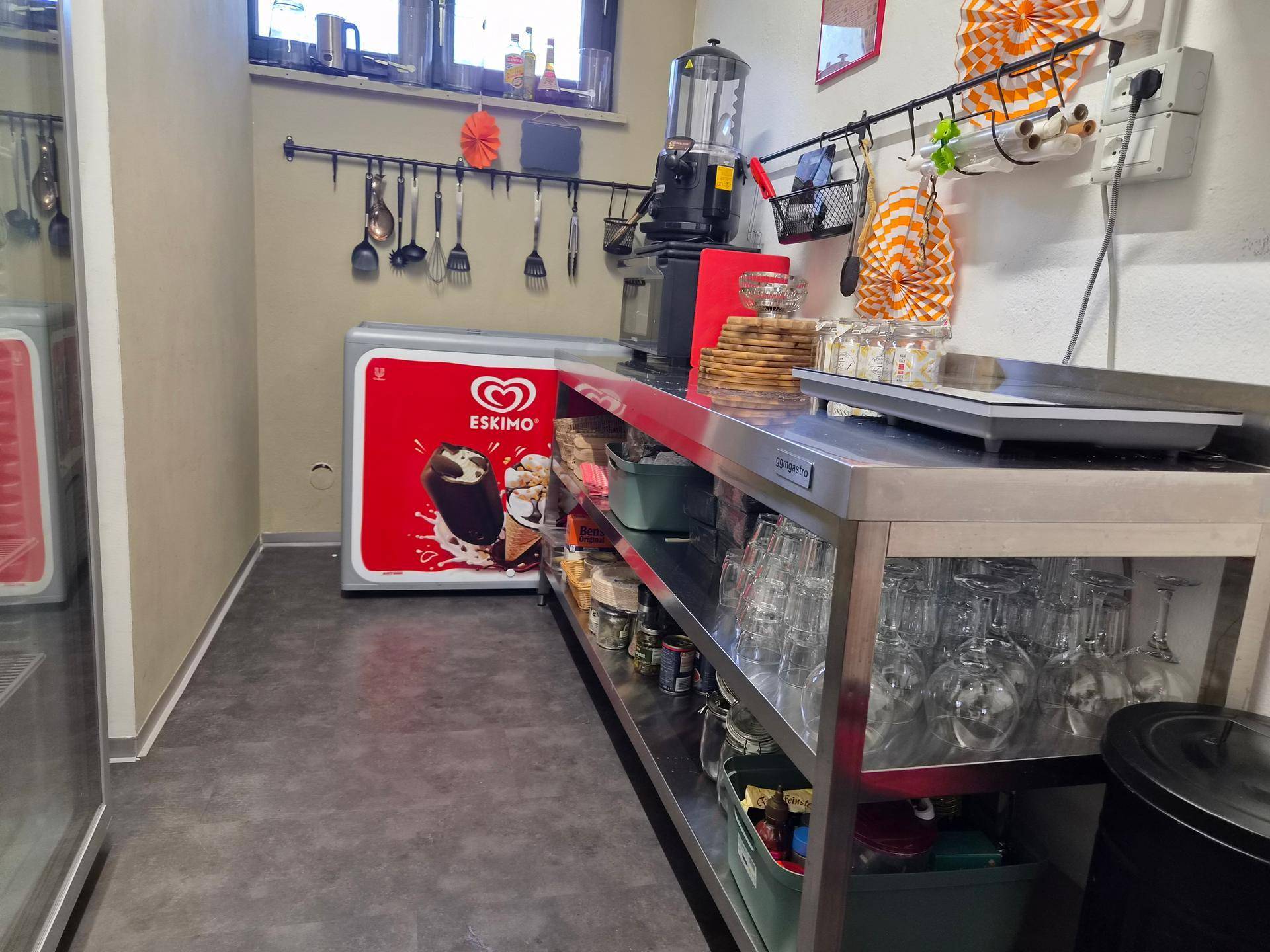 Gewerbliche Küche mit Edelstahlarbeitsflächen, einem Eisschrank und Utensilien an der Wand.