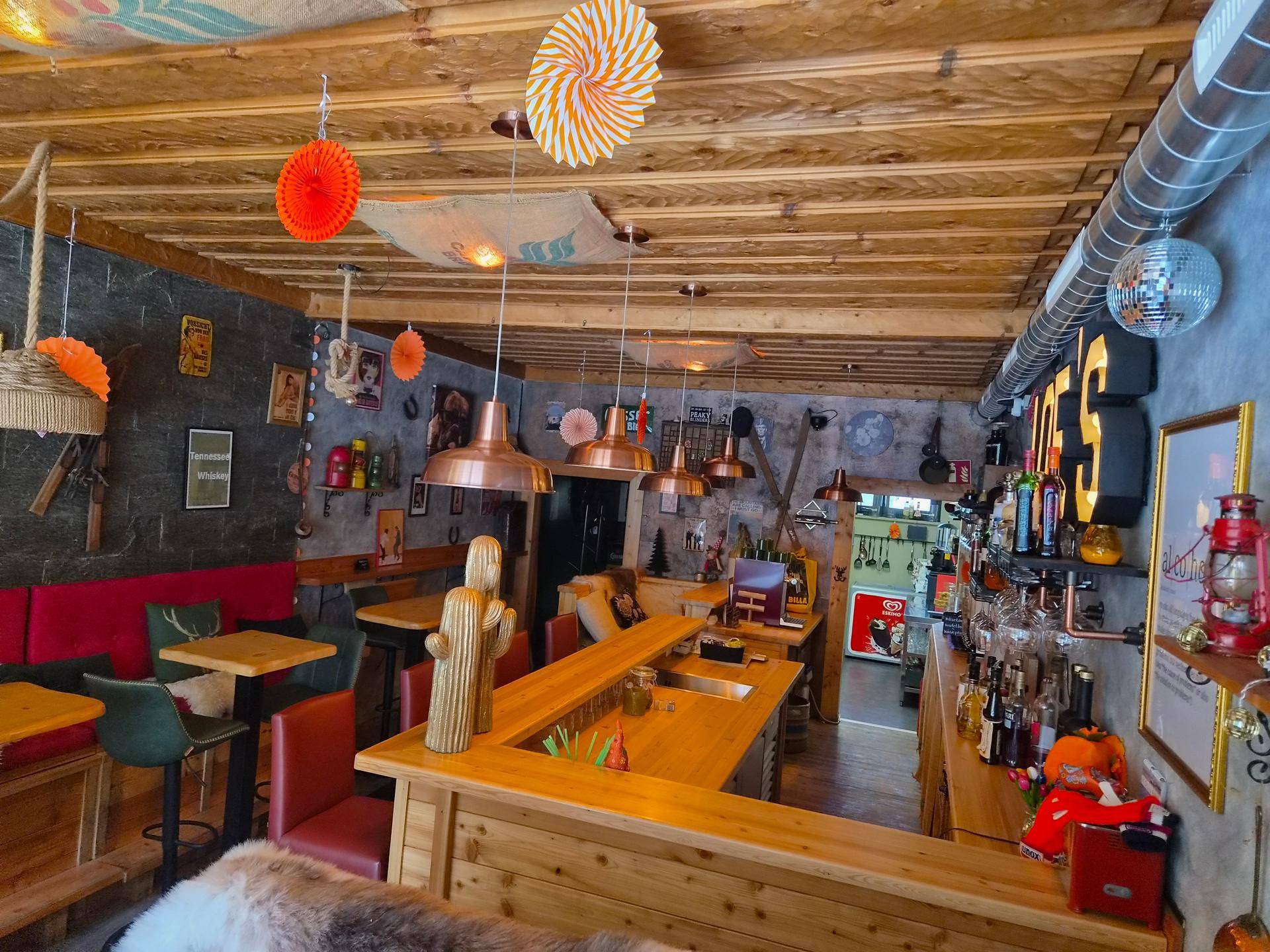 Weitläufiger Innenraum des Cafés mit Barbereich, Sitzgelegenheiten und auffälliger Decken- und Wanddekoration.