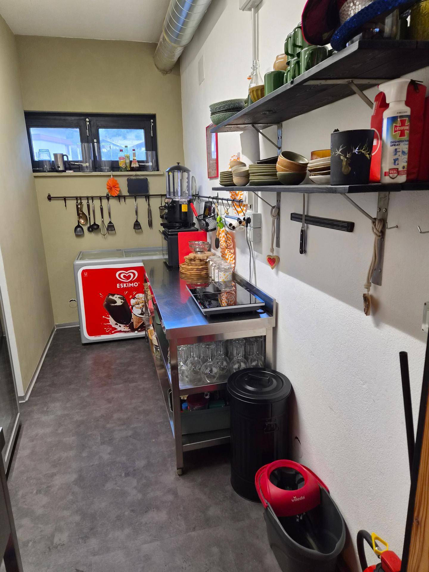 Gewerbliche Küche mit Edelstahlarbeitsflächen, Eisschrank und offenen Regalen für Geschirr.