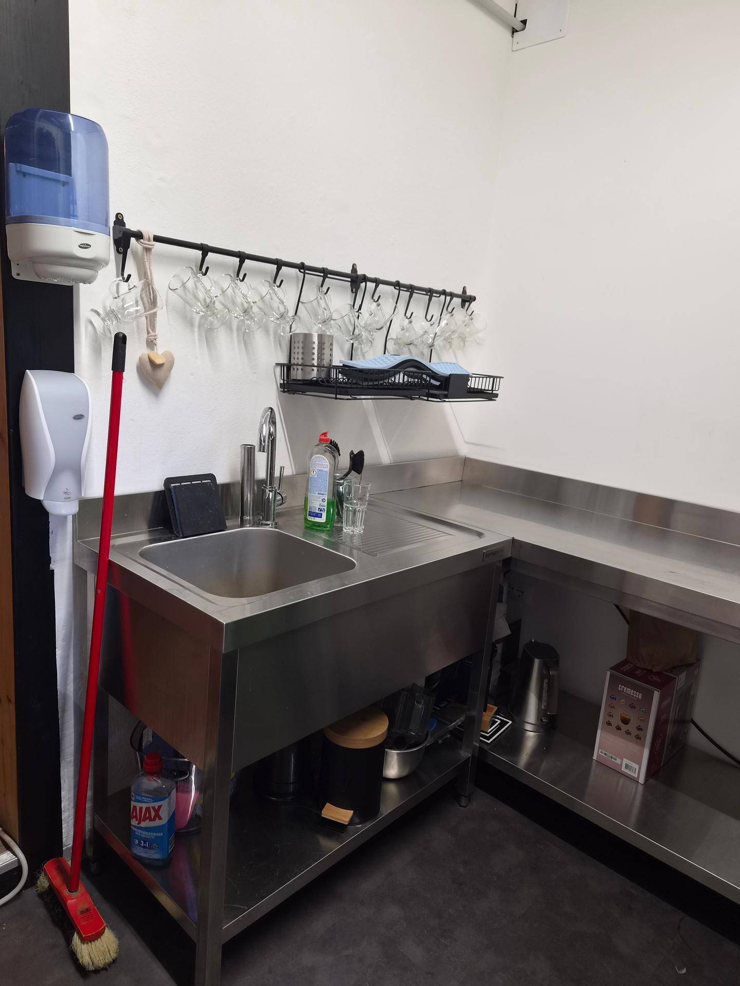 Nahaufnahme des Spülbereichs in der Gewerbeküche mit Edelstahlspüle und Wandhalterung für Gläser.