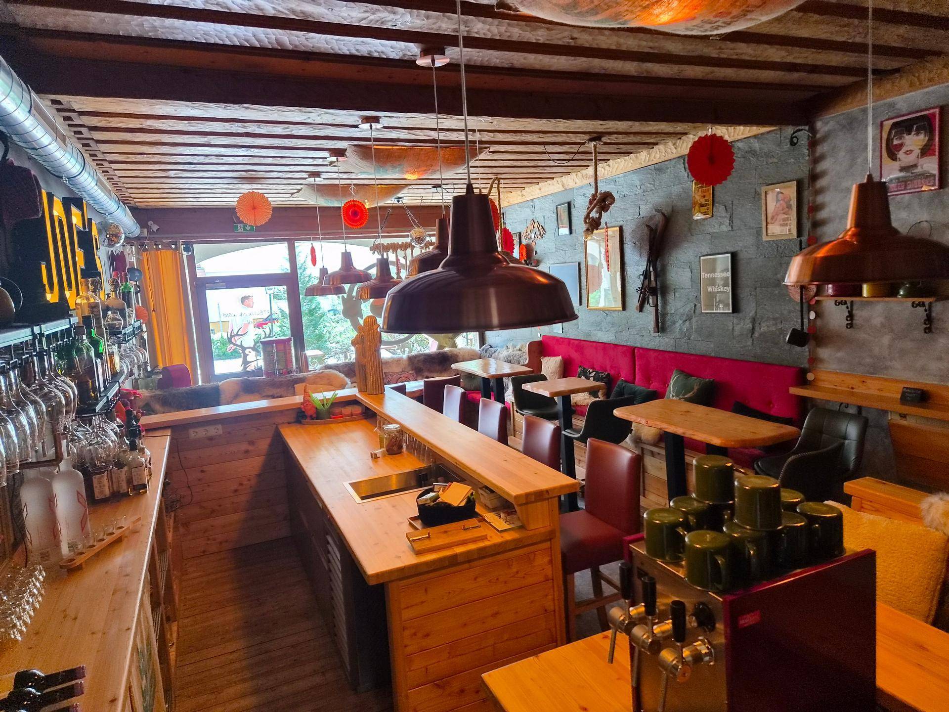 Blick auf den Barbereich mit Theke, Flaschenregalen und Sitzgelegenheiten, beleuchtet durch Fenster.