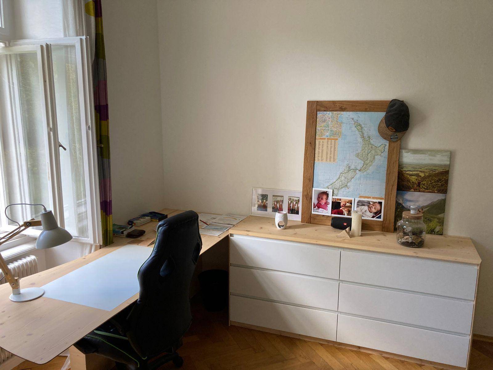 Heller Arbeitsbereich mit großem Schreibtisch, Bürostuhl und Kommode am Fenster.