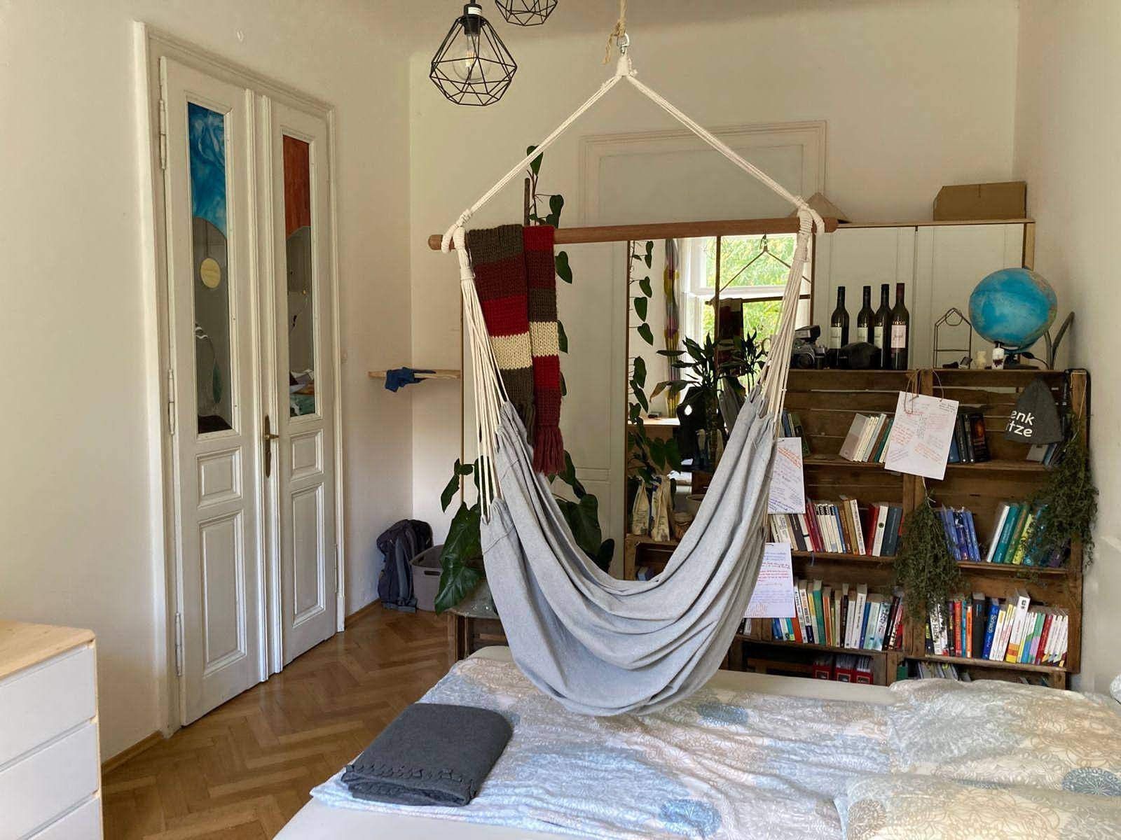 Gemütliches Schlafzimmer mit Hängesessel, Bücherregal aus Holzkisten und Parkettboden.