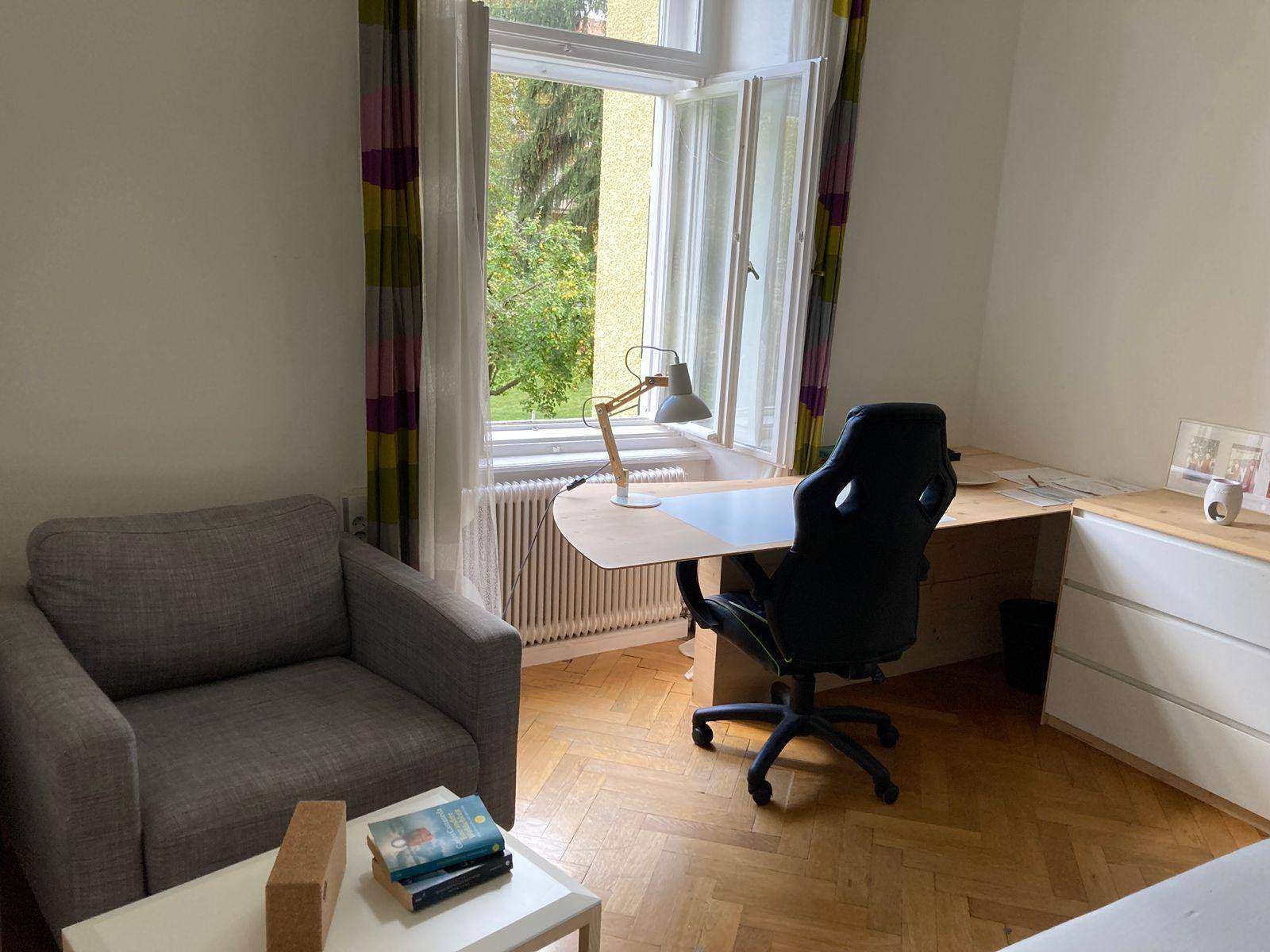 Arbeitszimmer mit Schreibtisch, bequemen Sessel und großem Fenster mit Blick ins Grüne.