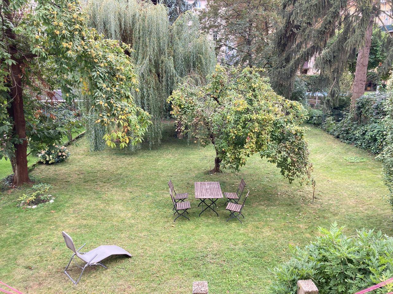 Grüner Garten mit Rasenfläche, Bäumen und einem kleinen Esstisch mit Stühlen.