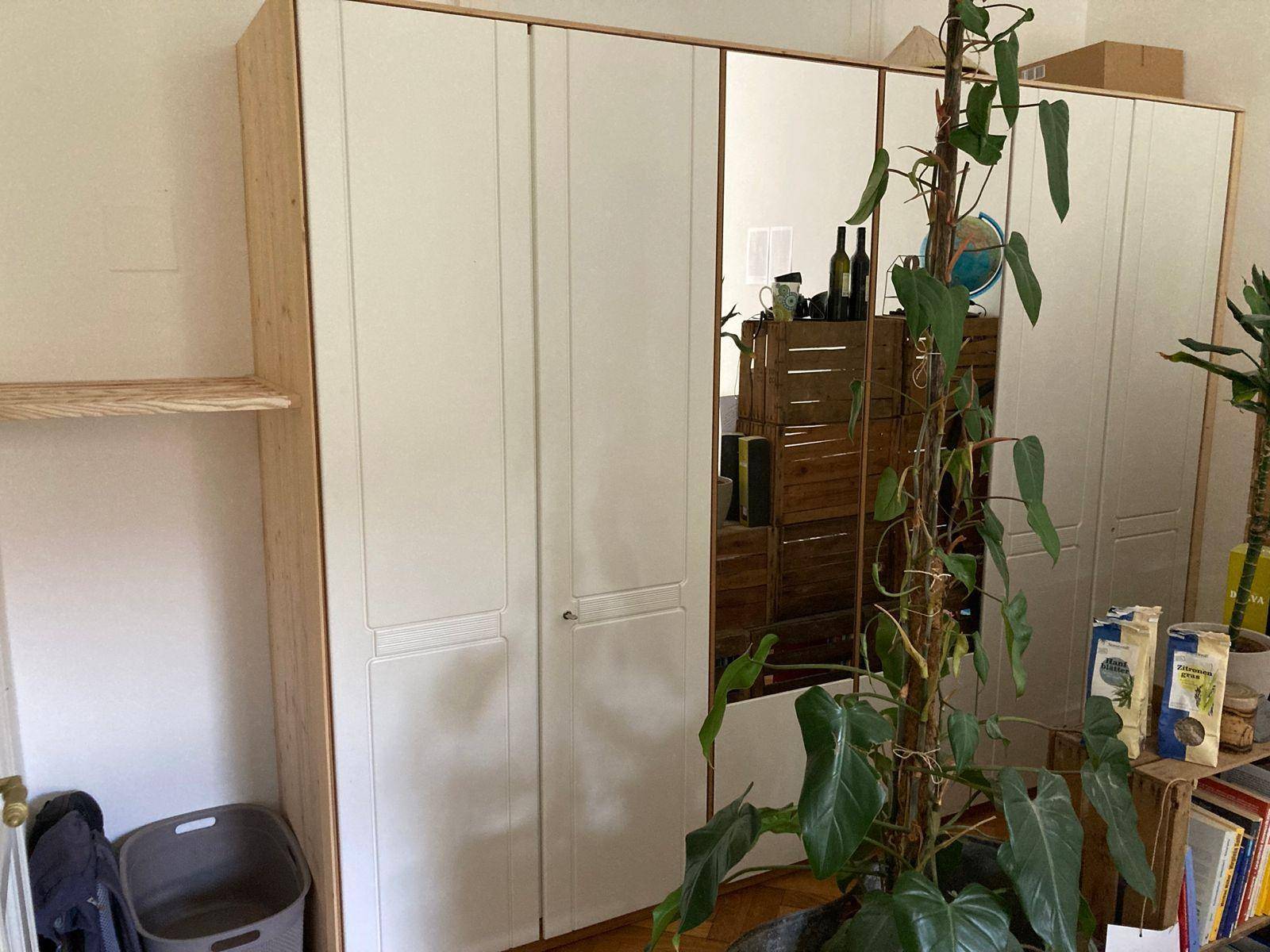 Heller Kleiderschrank mit Spiegeltüren und Holzrahmen in einem Schlafzimmer.