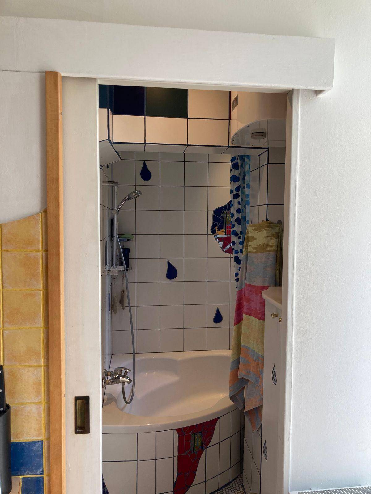 Kleines Badezimmer mit Eckbadewanne und farbenfrohen Fliesen in einem verspielten Design.