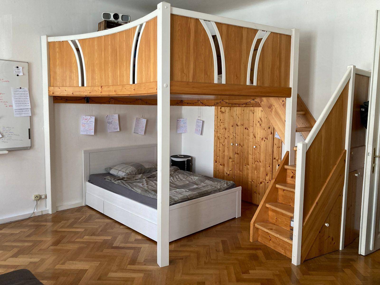 Helles Schlafzimmer mit Hochbettkonstruktion, Holztreppe und einem großen Whiteboard an der Wand.