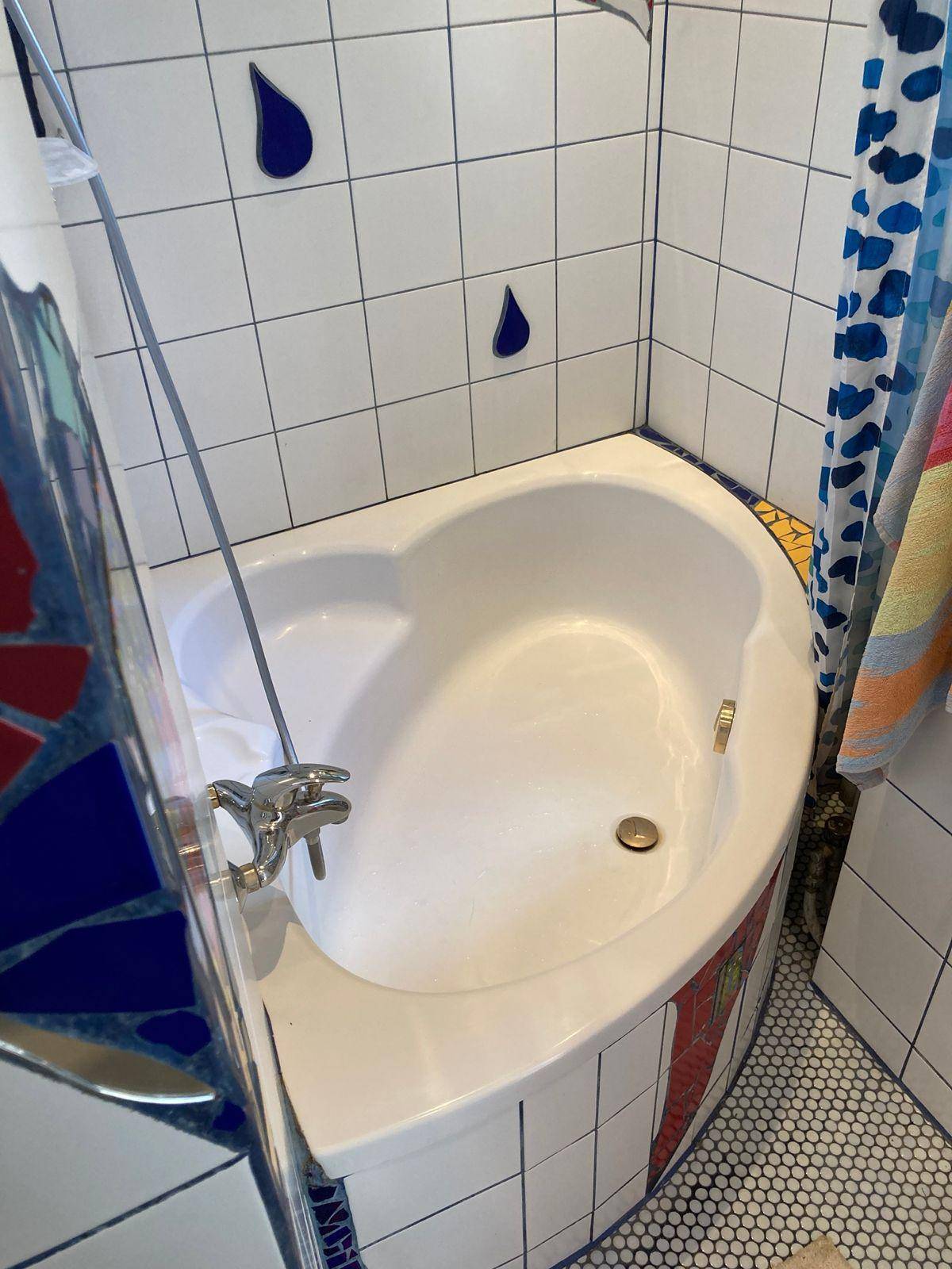 Nahaufnahme der Eckbadewanne mit Duschfunktion und den auffälligen, farbigen Fliesen.